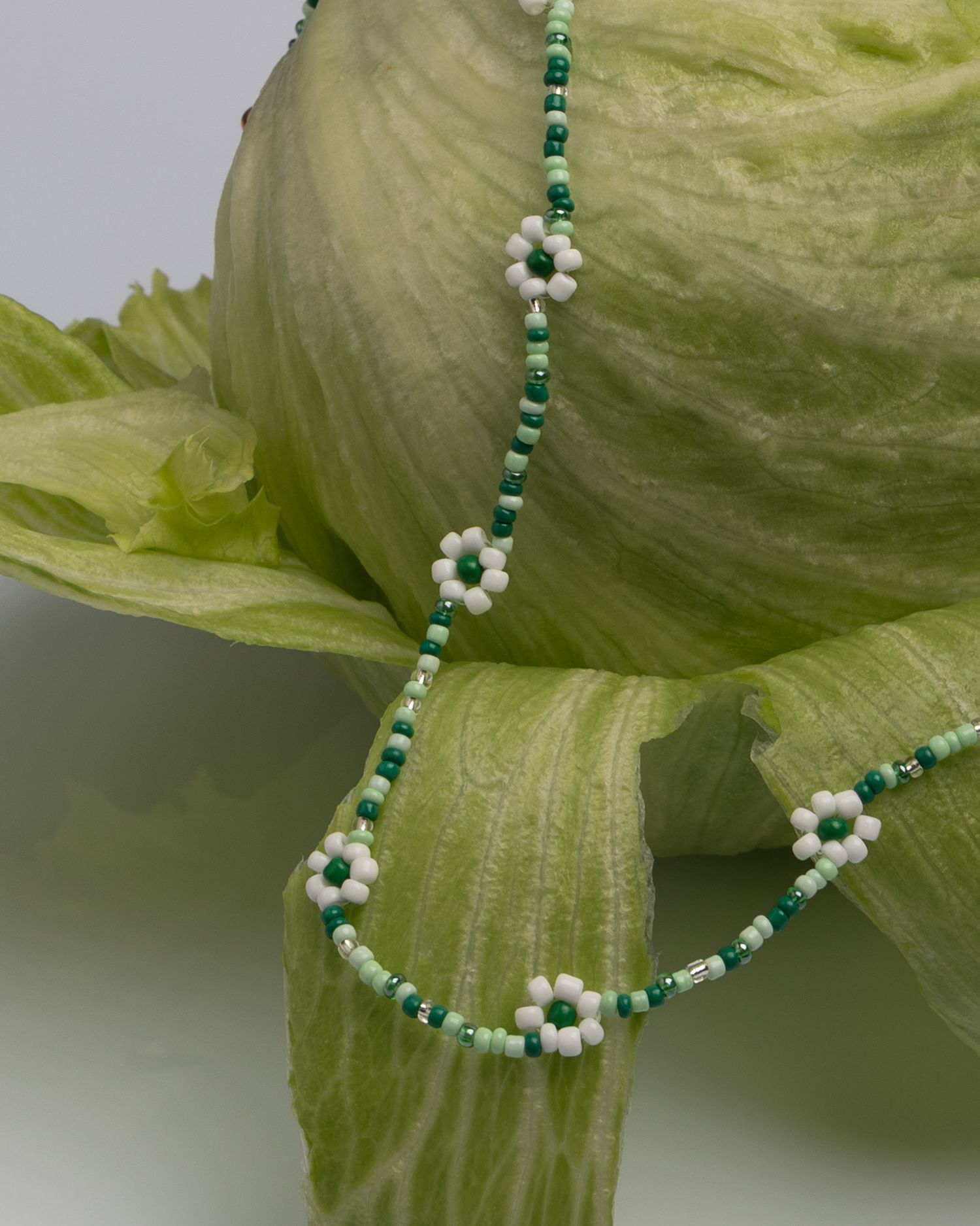 Delicate beaded necklace featuring turquoise and white daisy flower patterns against green leafy background.