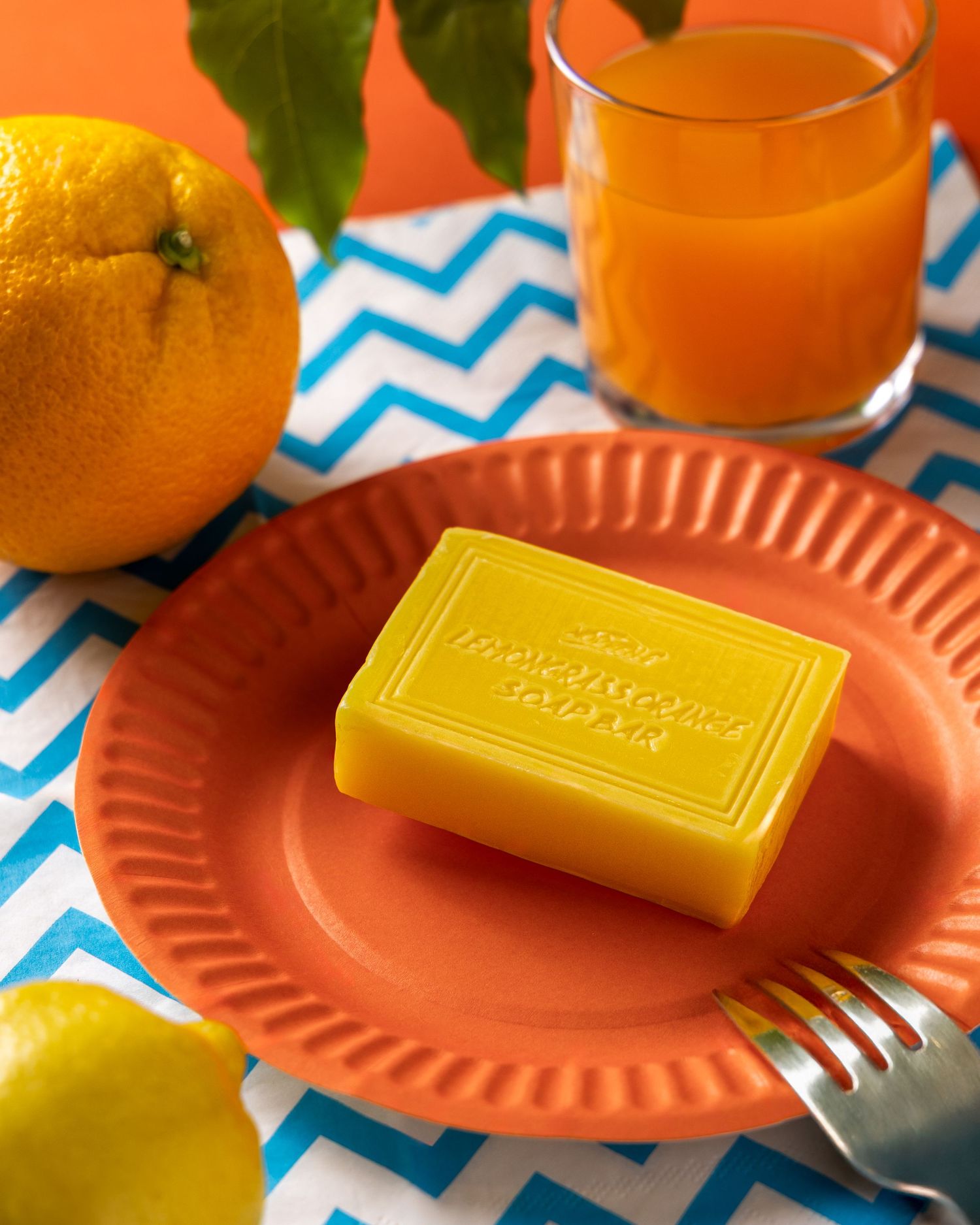 Fresh oranges and a glass of orange juice arranged on coral colored plates with blue chevron pattern background.