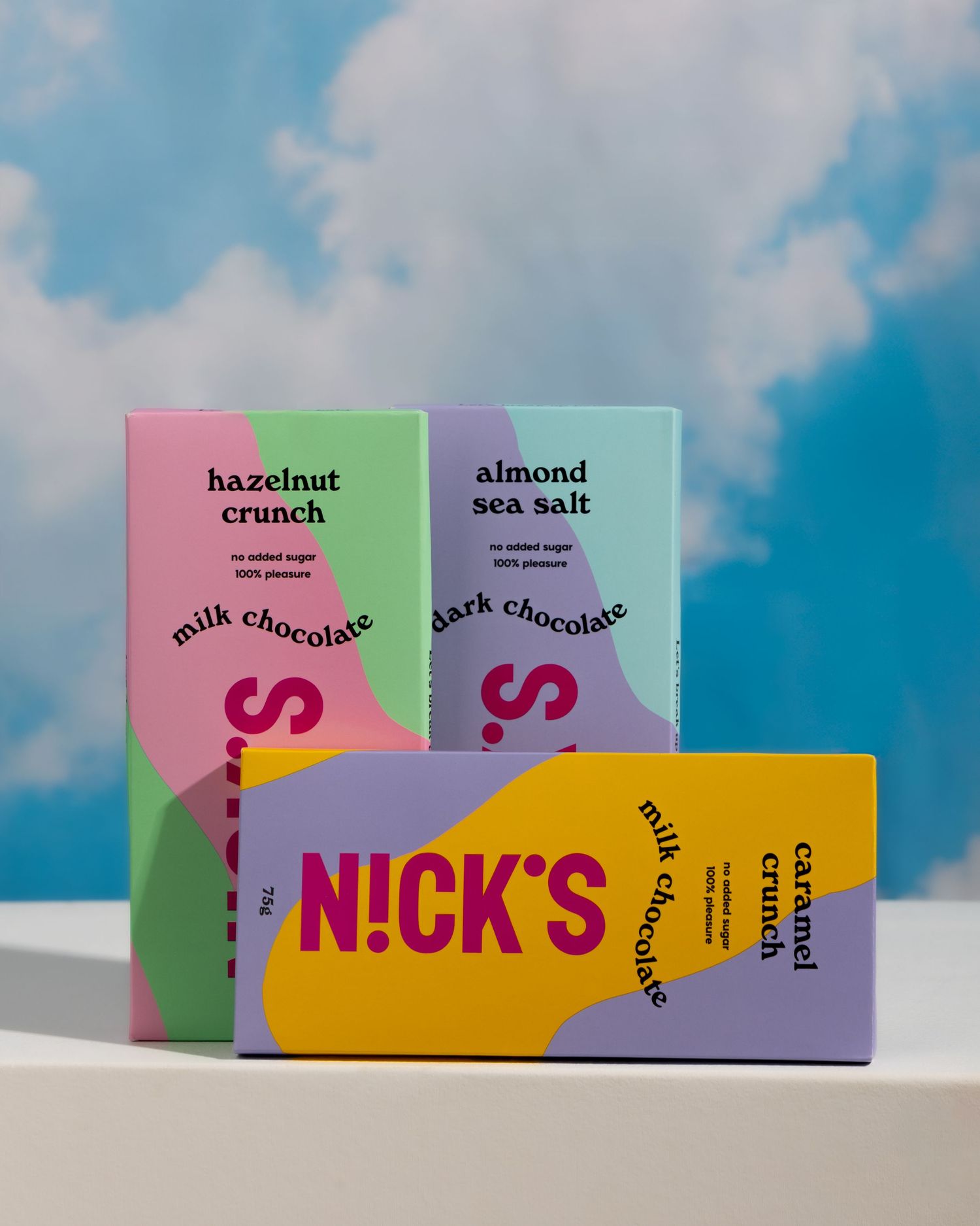 Three colorful chocolate bars from Nick's in hazelnut crunch, almond sea salt, and milk chocolate flavors against a cloudy sky.