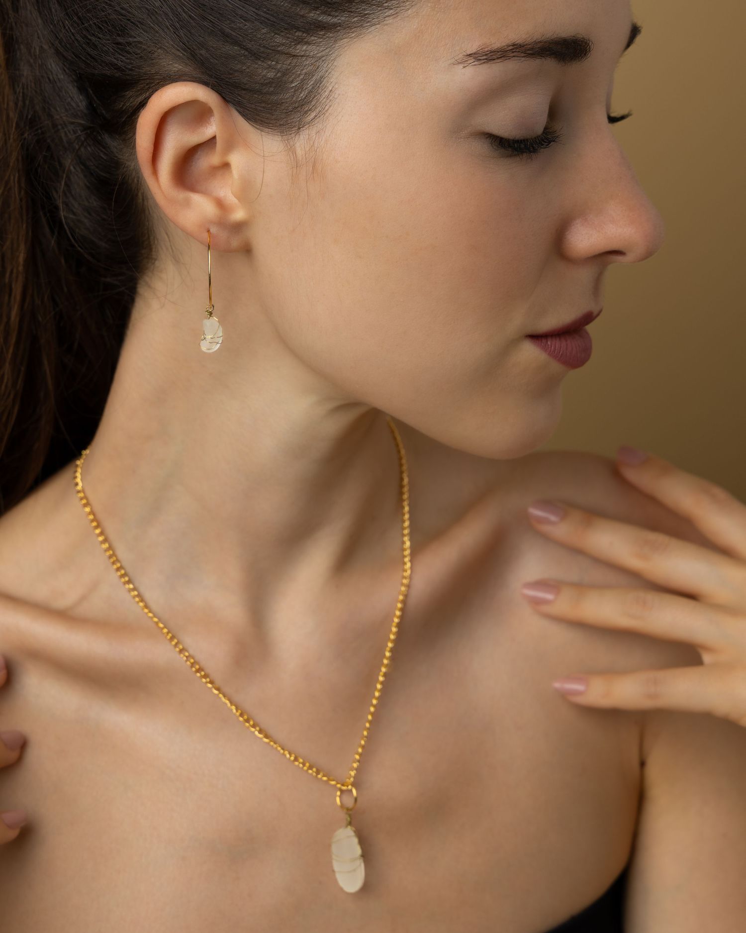 Gold chain necklace with crystal pendant displayed at different angles against warm brown background.