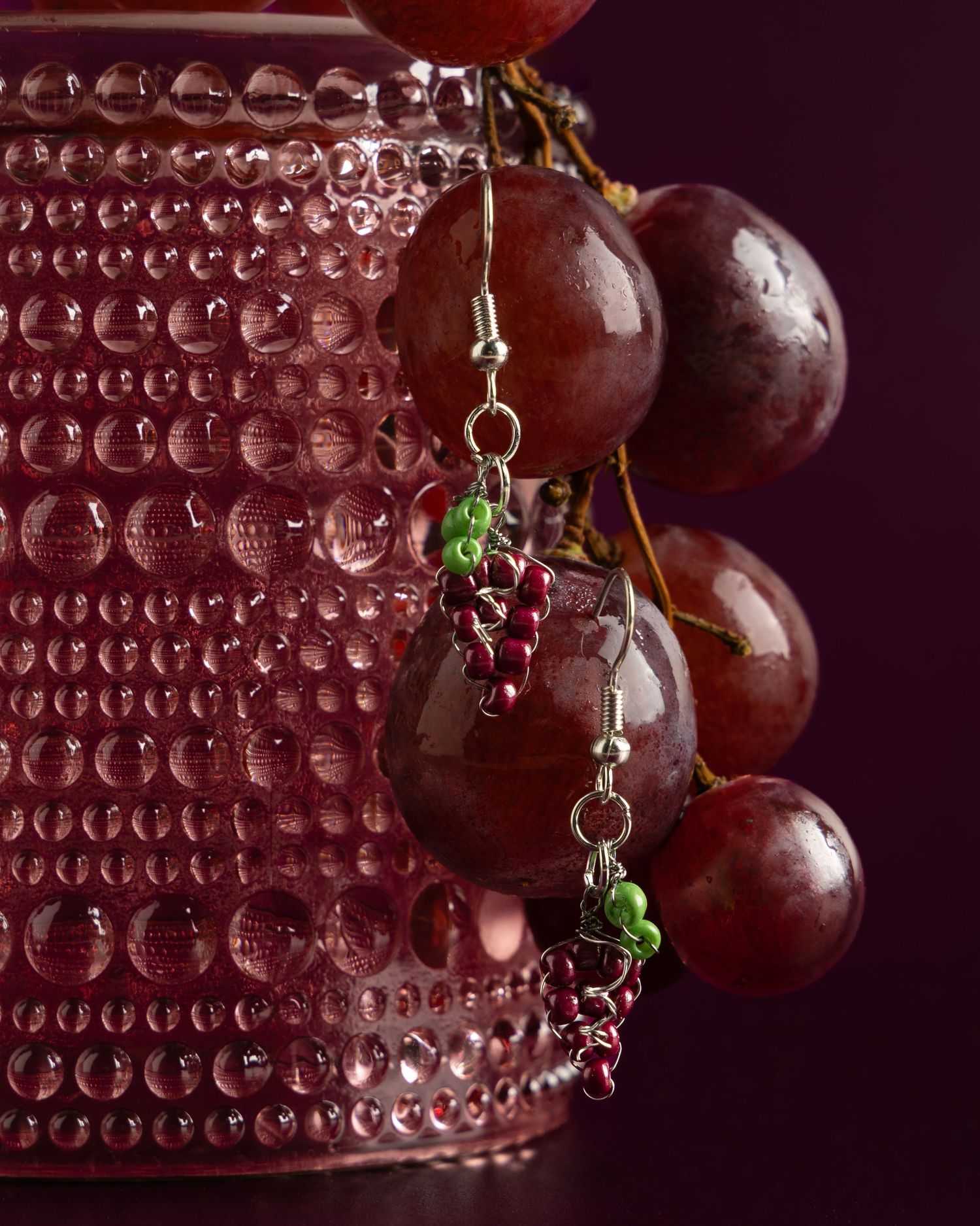 Fresh red grapes with water droplets hanging beside a textured pink glass surface in elegant macro photography.