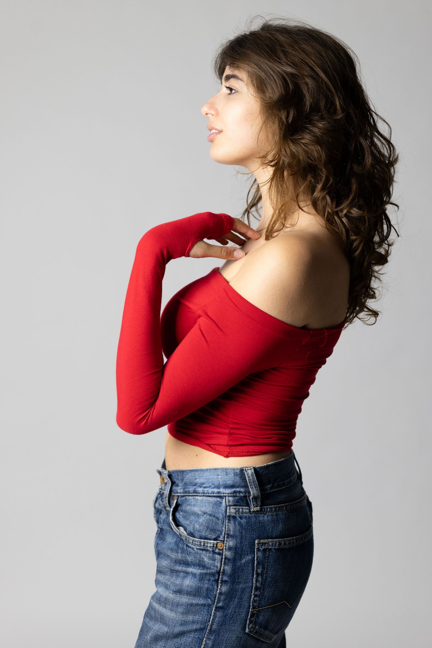 Side profile in red off-shoulder top and denim against grey background.