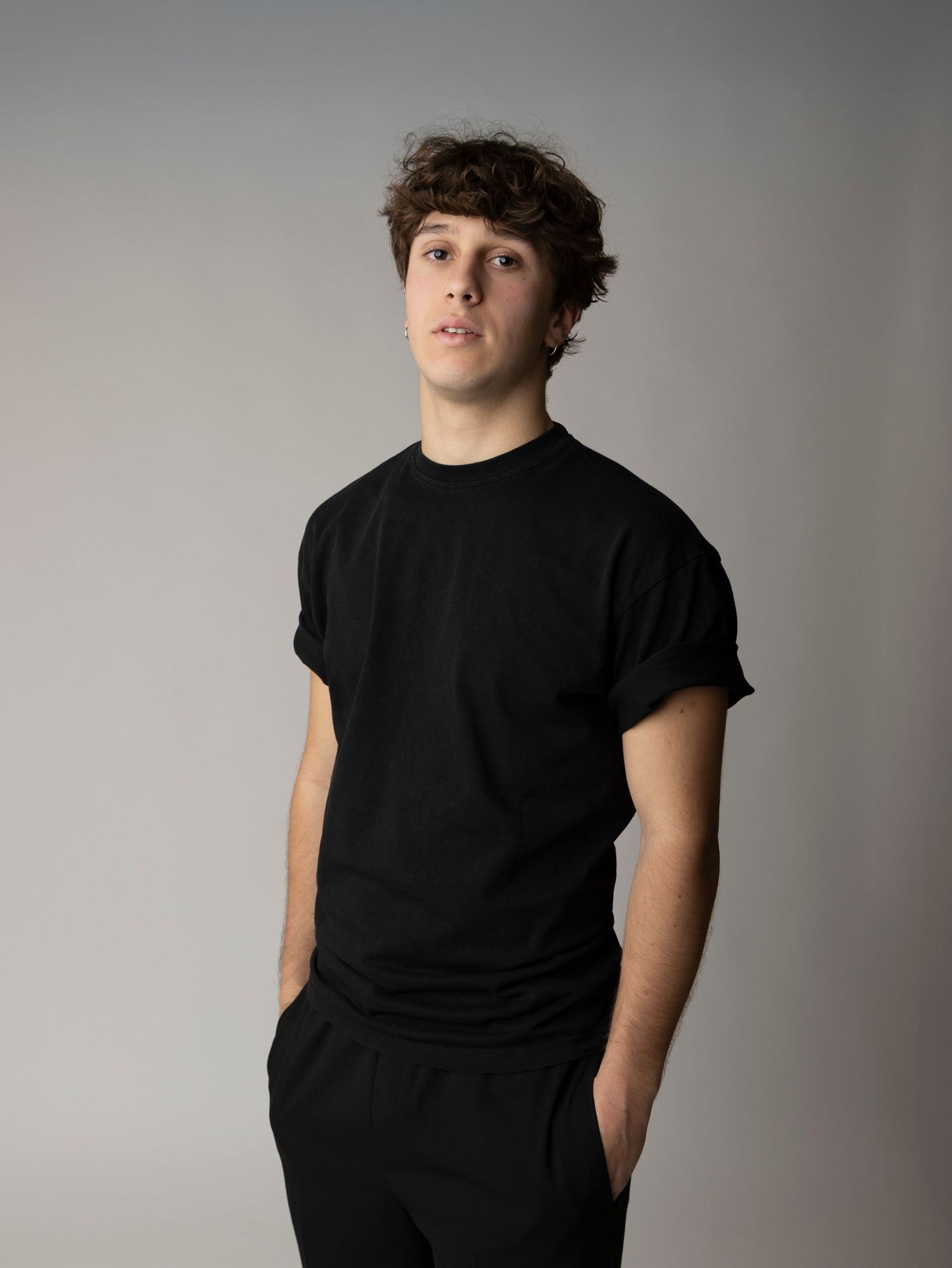 A figure in a black t-shirt poses against a gray studio backdrop in a series of artistic portraits.