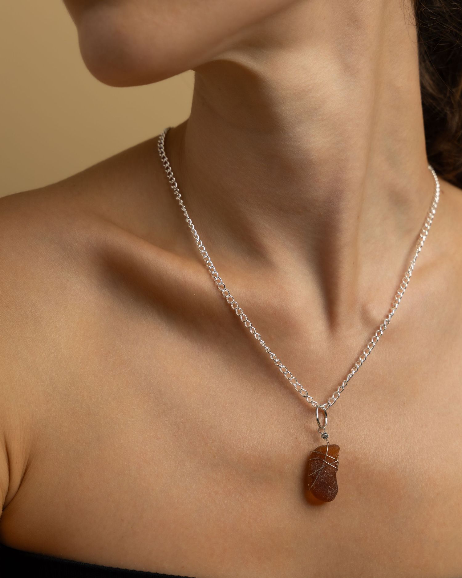 Nine close-up shots of a necklace with a polished tiger's eye stone pendant on a silver chain.