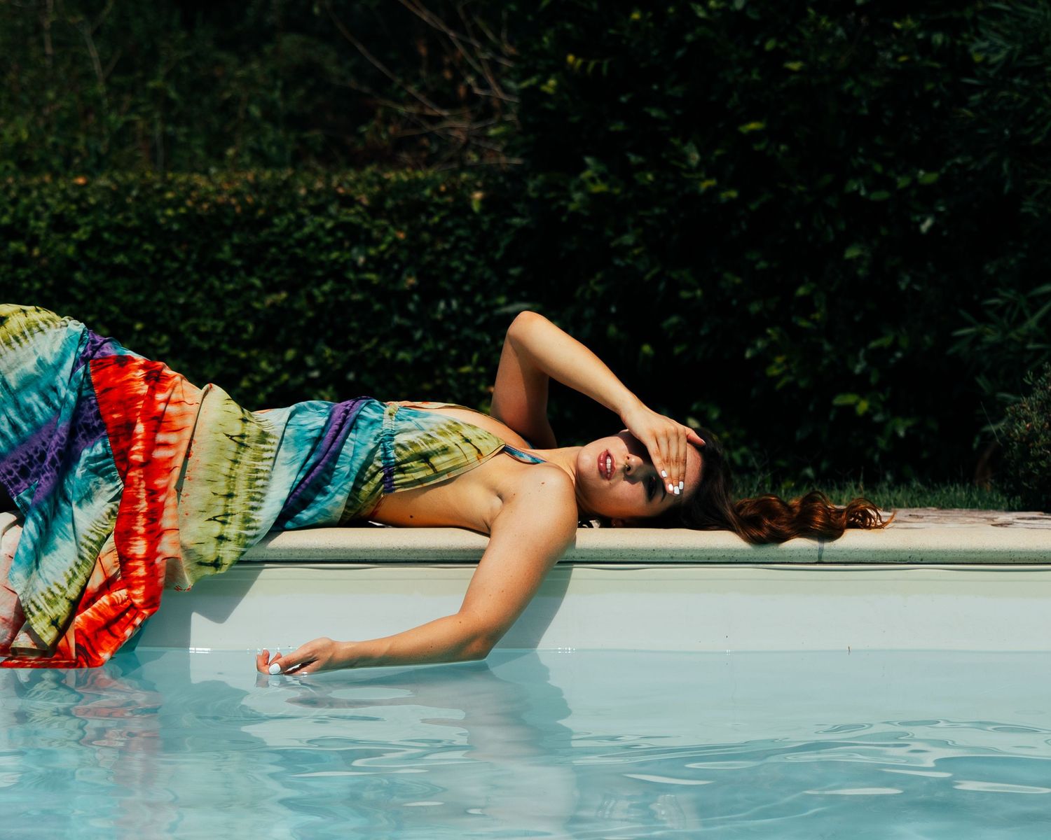 Person in colorful swimsuit floating and splashing in bright blue swimming pool on sunny summer day.