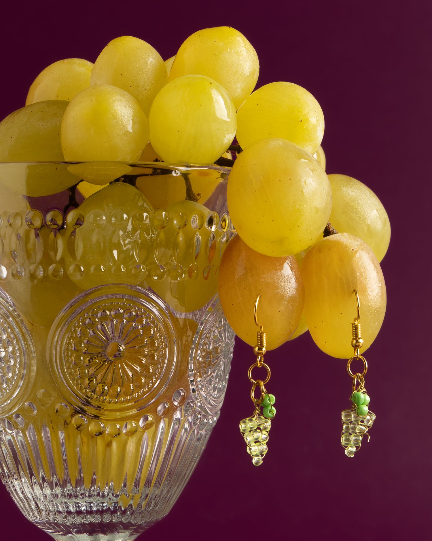 Fresh yellow grapes hanging over a decorative crystal bowl against a deep purple background.