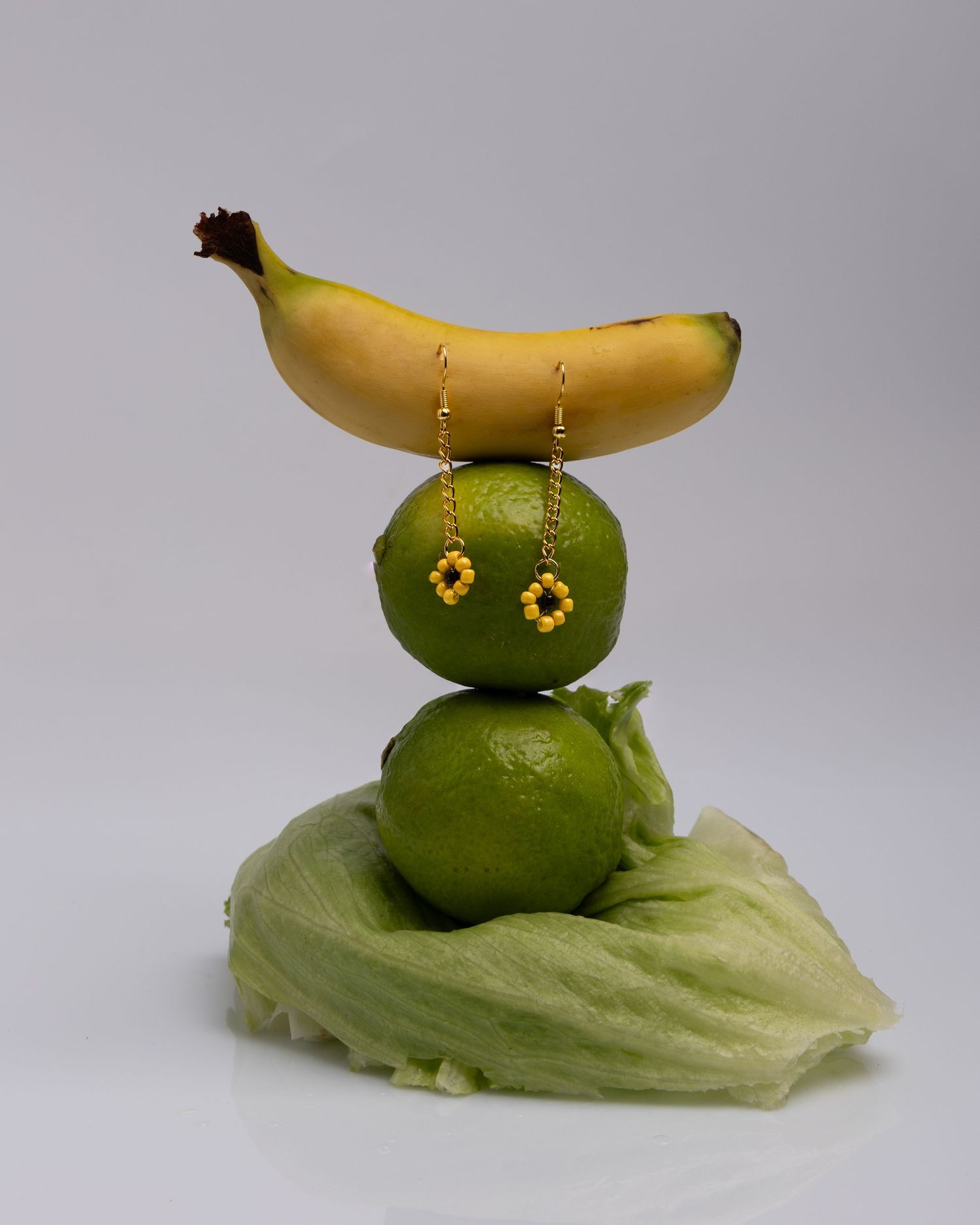 A creative food art sculpture made with two limes stacked on lettuce and topped with a banana resembling a whimsical creature.