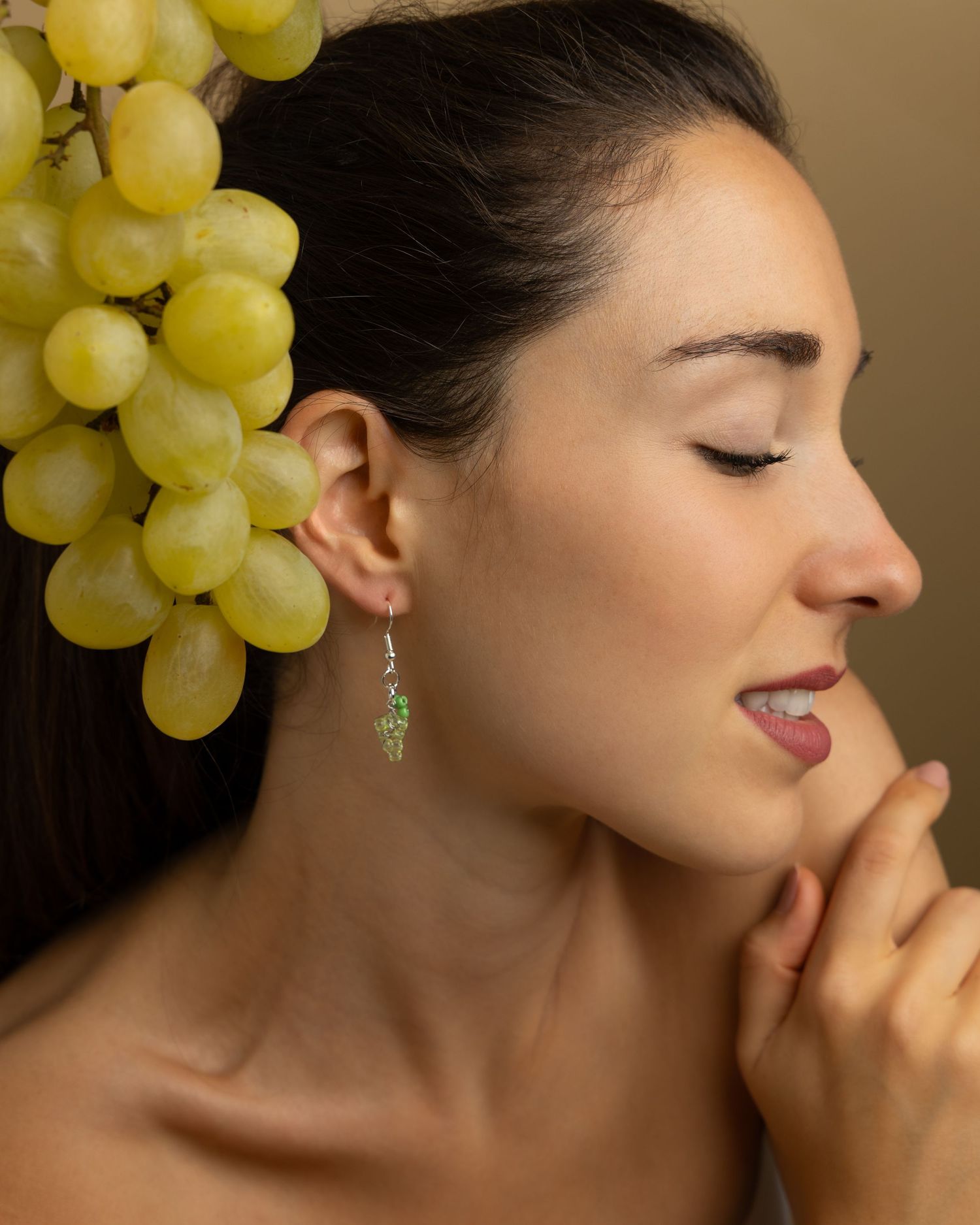 Creative portrait showing a person in profile adorned with fresh green grapes and leaf-shaped earrings.