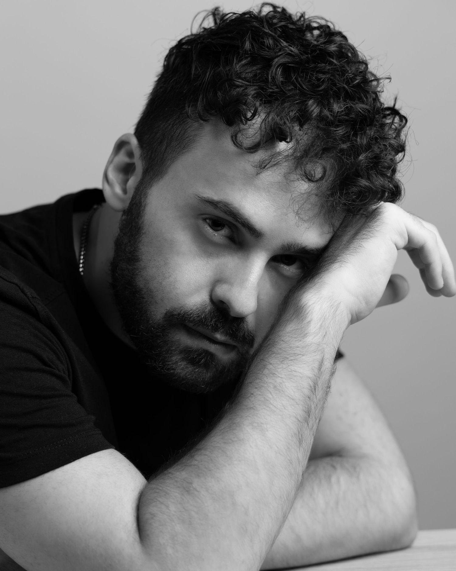 A series of monochromatic self-portraits showing a contemplative figure resting head in hand in various poses against a gray backdrop.