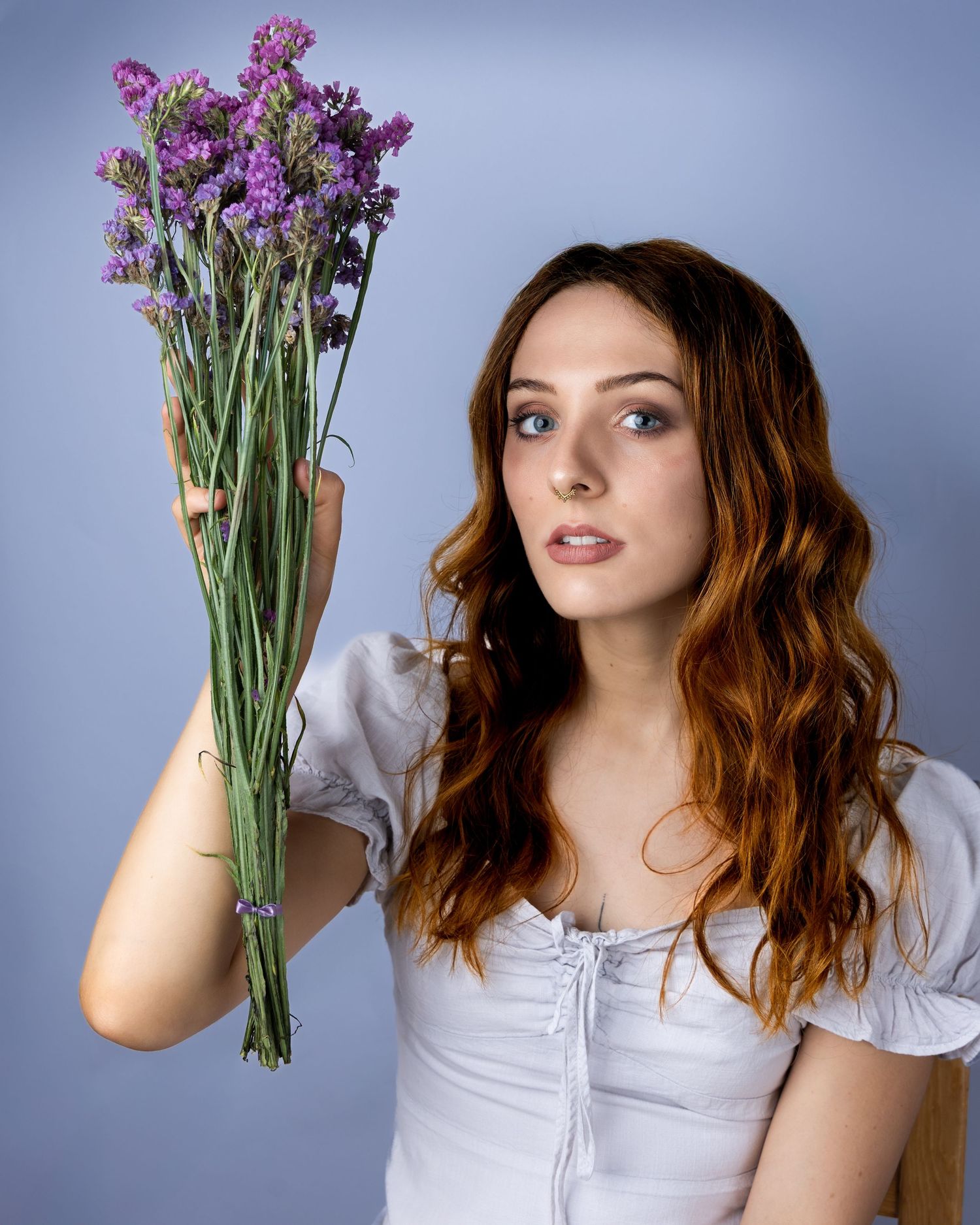 Model in a white top holding a bouquet of purple wildflowers against a blue background.