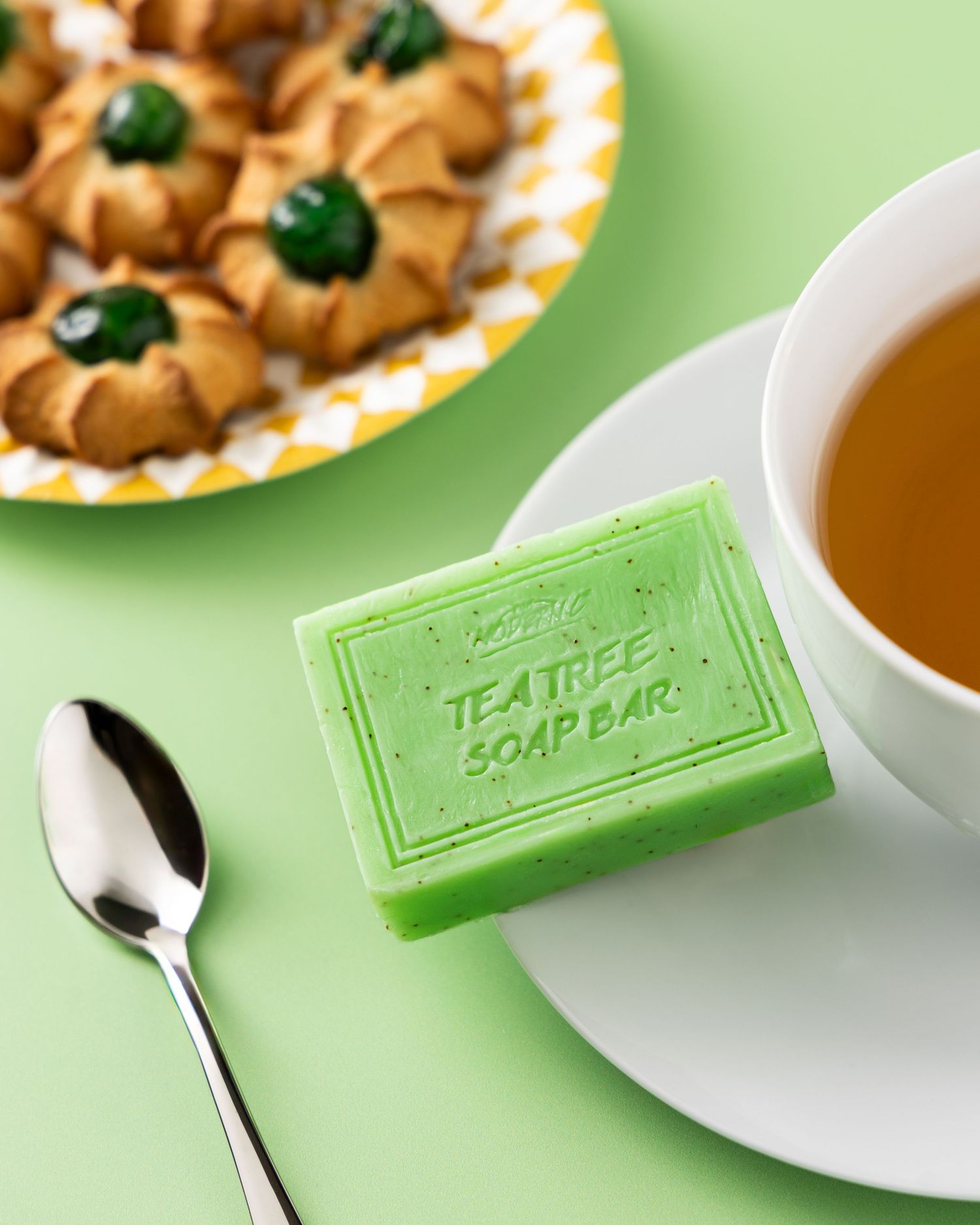 Tea tree soap bar with soft focus cup of tea and cookies in pastel green background.
