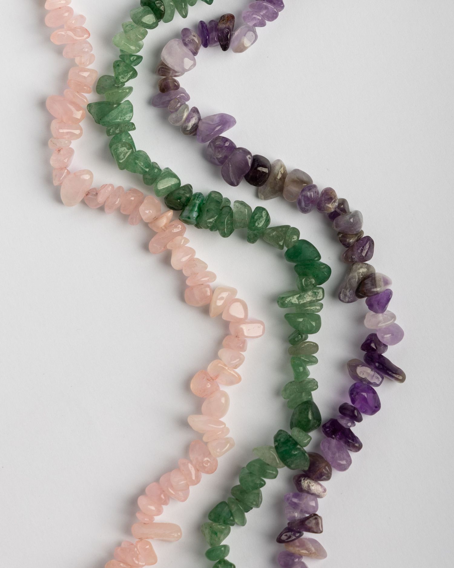 Three diagonal rows of crystal beads in pink, green, and purple amethyst on a white background.