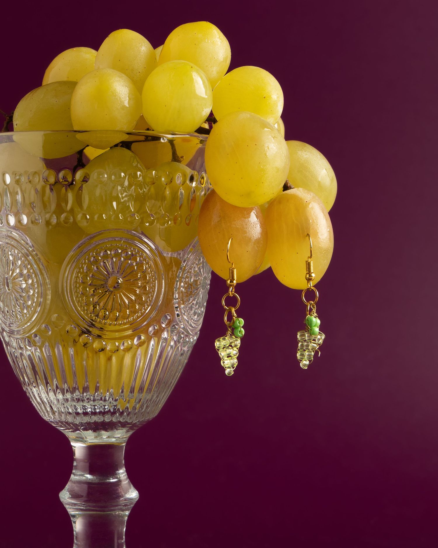 Fresh yellow grapes arranged in an ornate vintage glass goblet against a dark purple background.