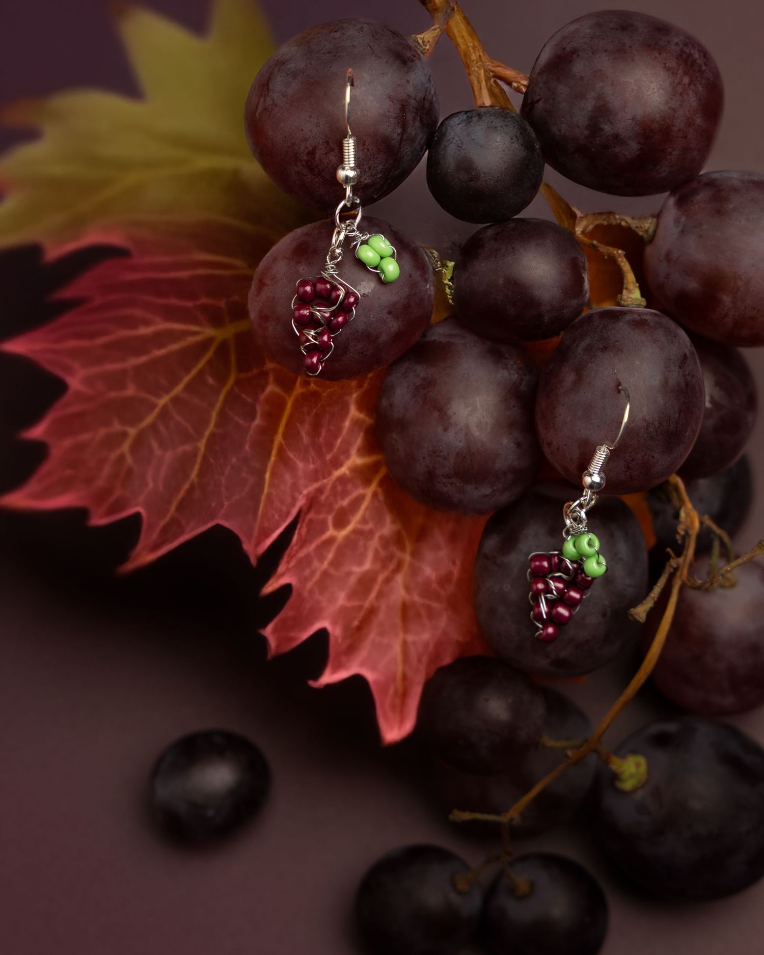 Purple grapes and autumn leaves artfully arranged with delicate earrings featuring grape cluster designs.