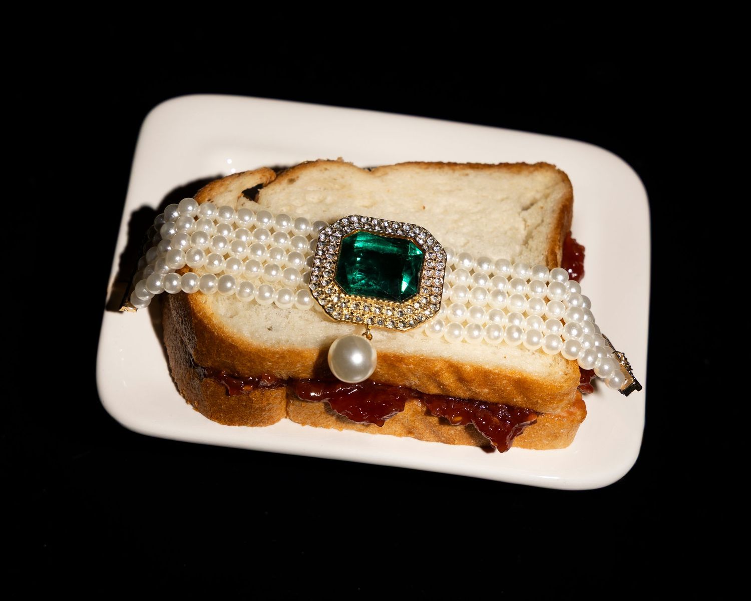 Elegant vintage brooch with emerald green stone and pearl accents displayed on white surface against black background.