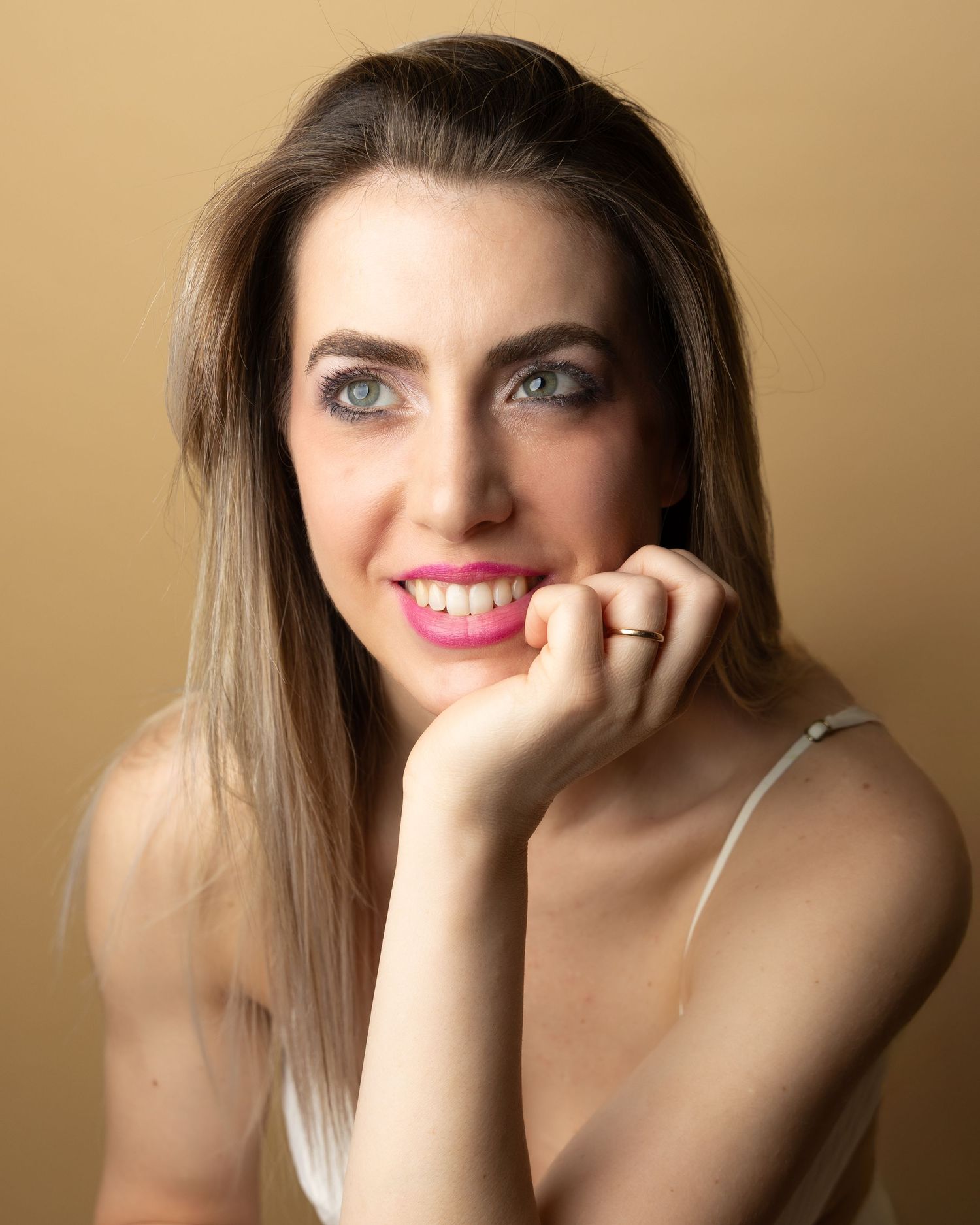 A beauty portrait features bright blue eyes, white smile, and ombre hair against a warm beige background.