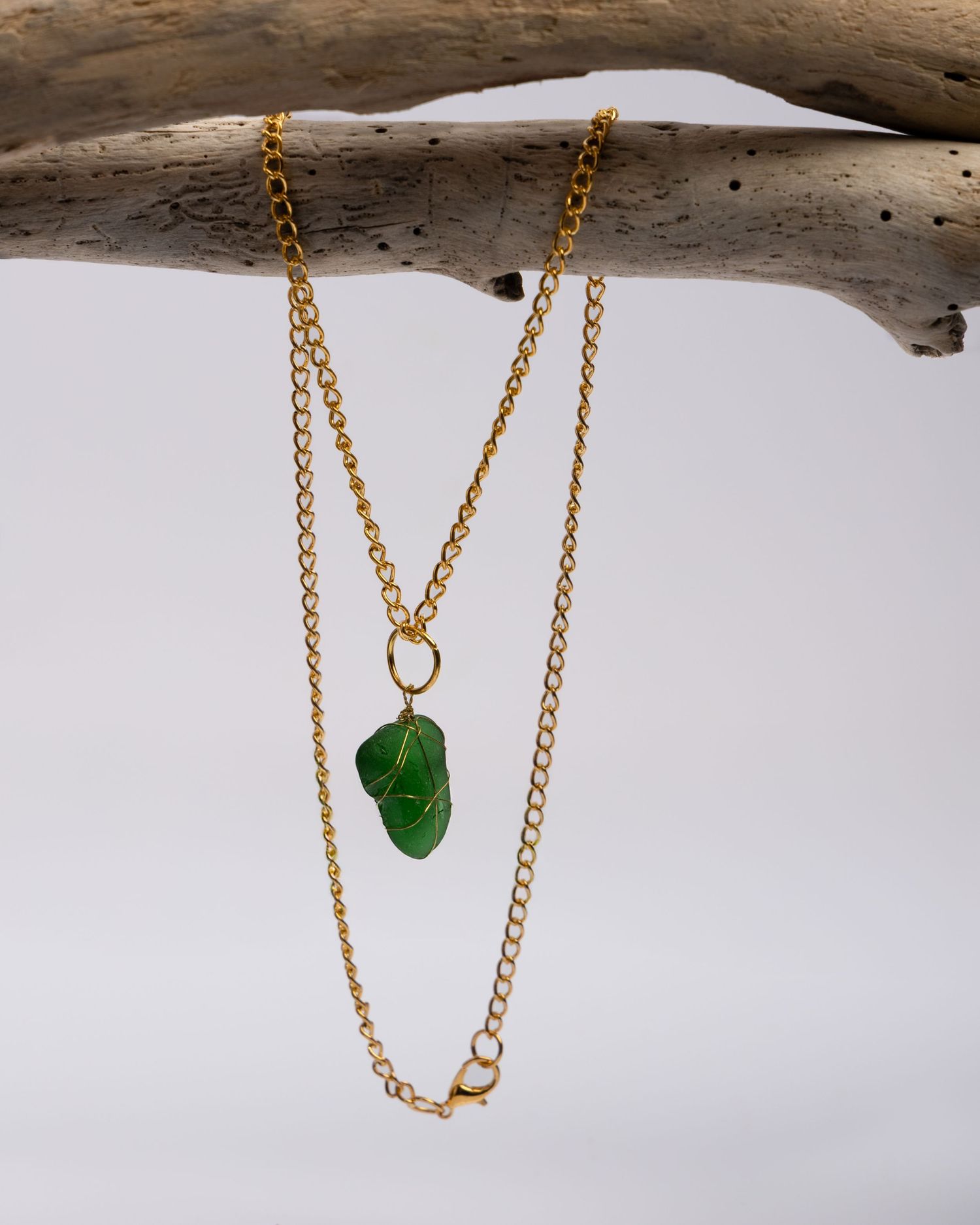 Four minimalist dainty gold necklaces with delicate green sea glass pendants displayed on driftwood against white background.
