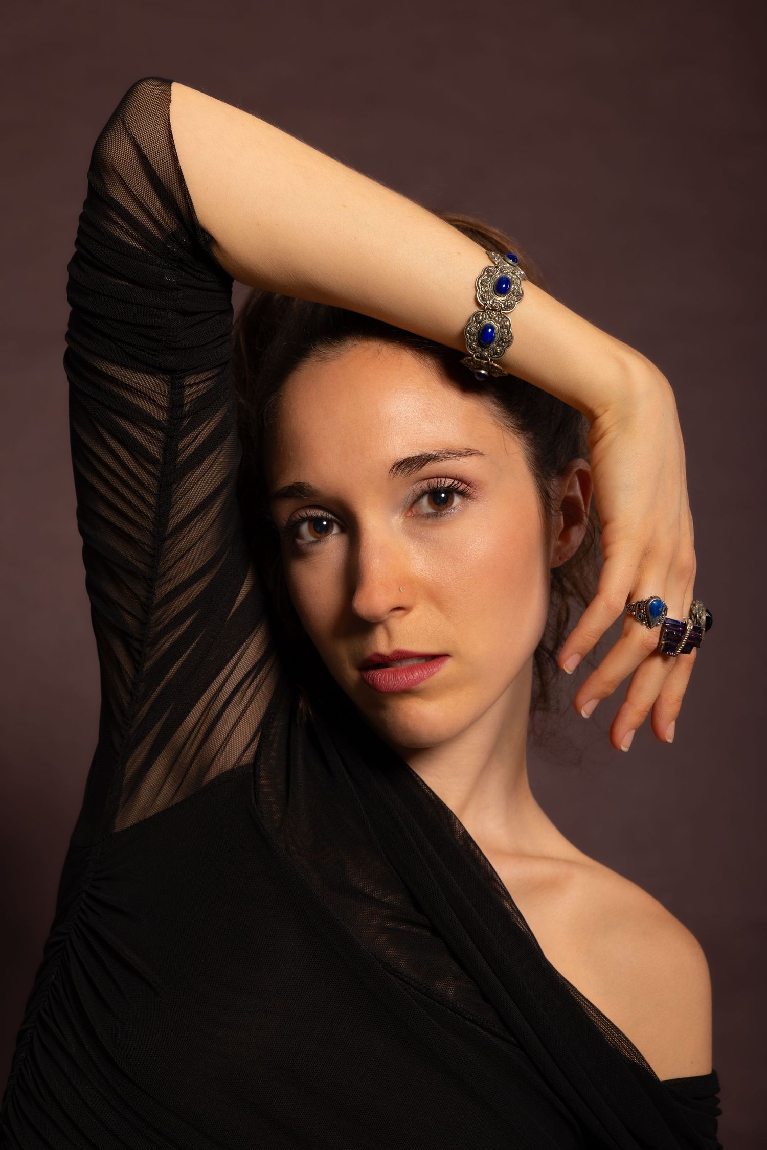 Studio portrait showing jewelry and sheer black clothing against dark background.