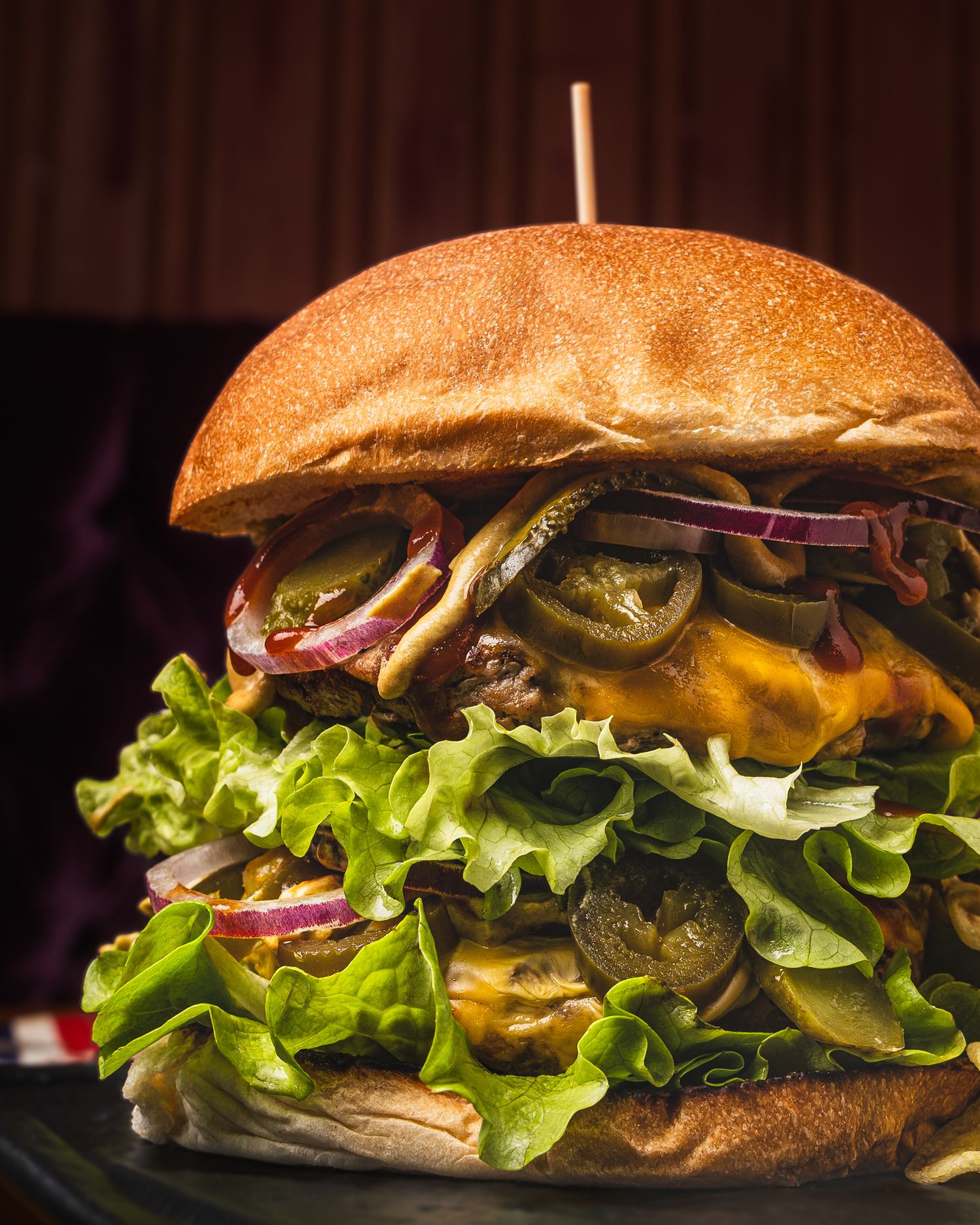 A towering gourmet cheeseburger with jalapenos, melted cheese, fresh lettuce and multiple layers on a golden brioche bun.