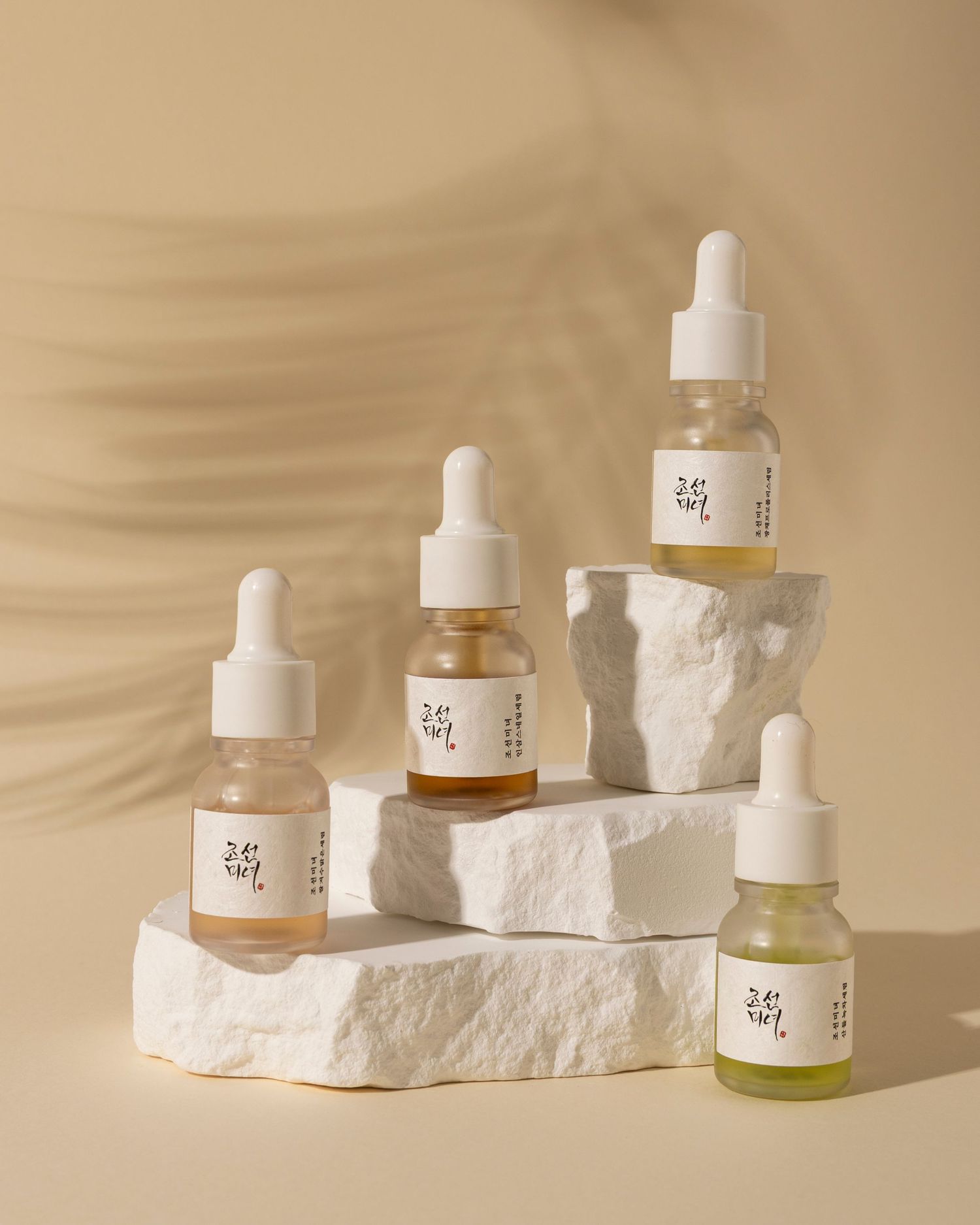 Glass dropper bottles of skincare serum arranged on white stone platforms against a beige background.