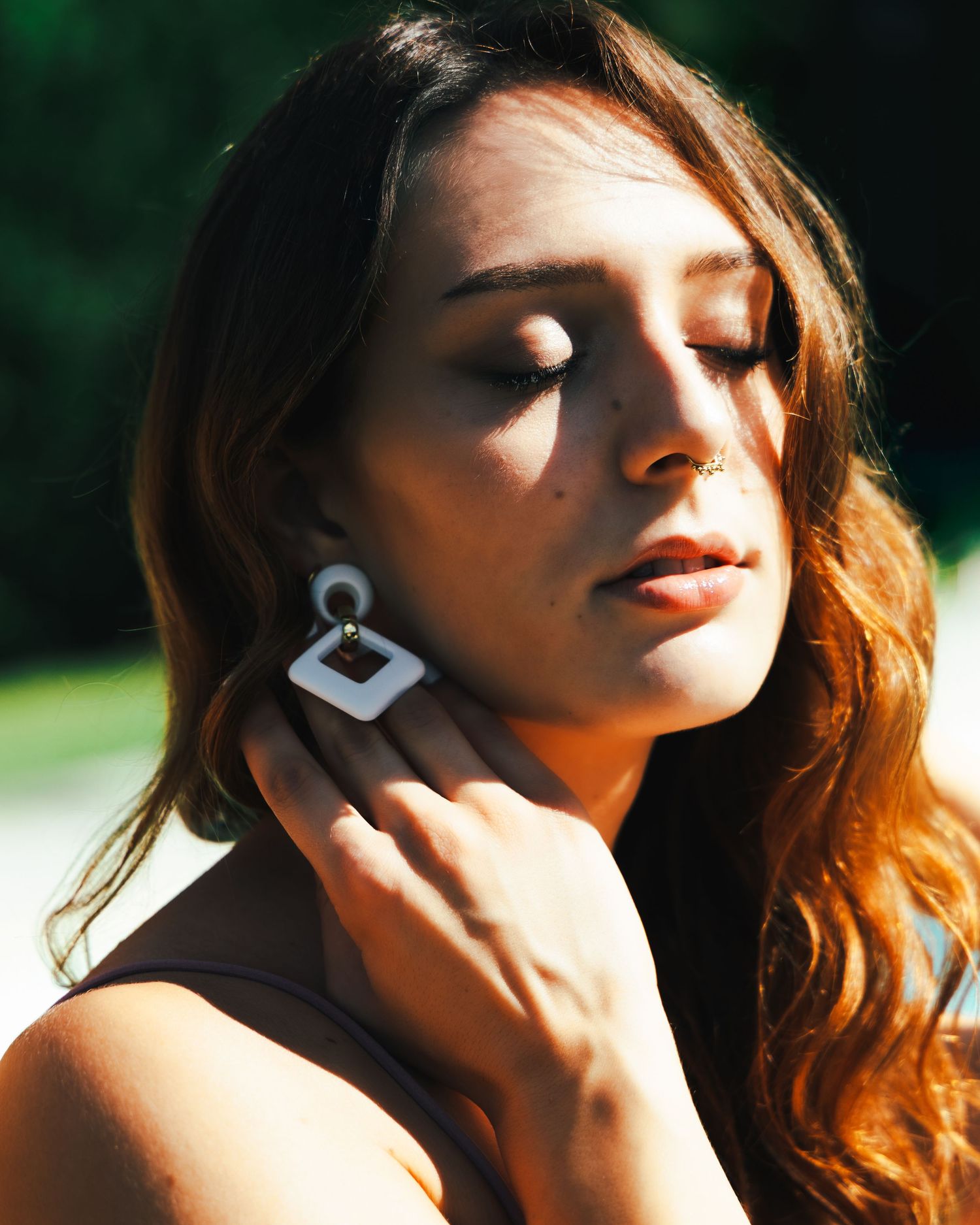Artistic portrait series featuring a woman with wavy hair in dramatic sunlight posing against a blurred natural background.