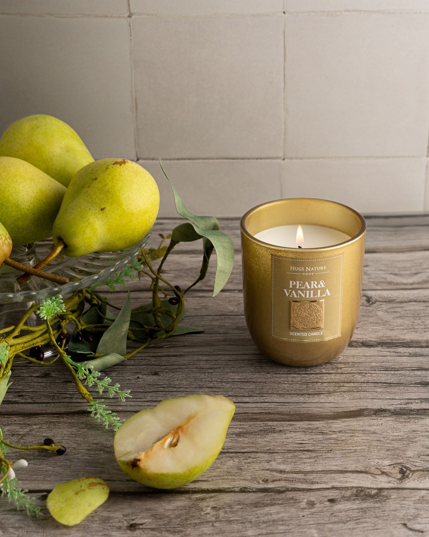 Gold candle with fresh green pears and leaves arranged on rustic wooden surface in minimalist style.