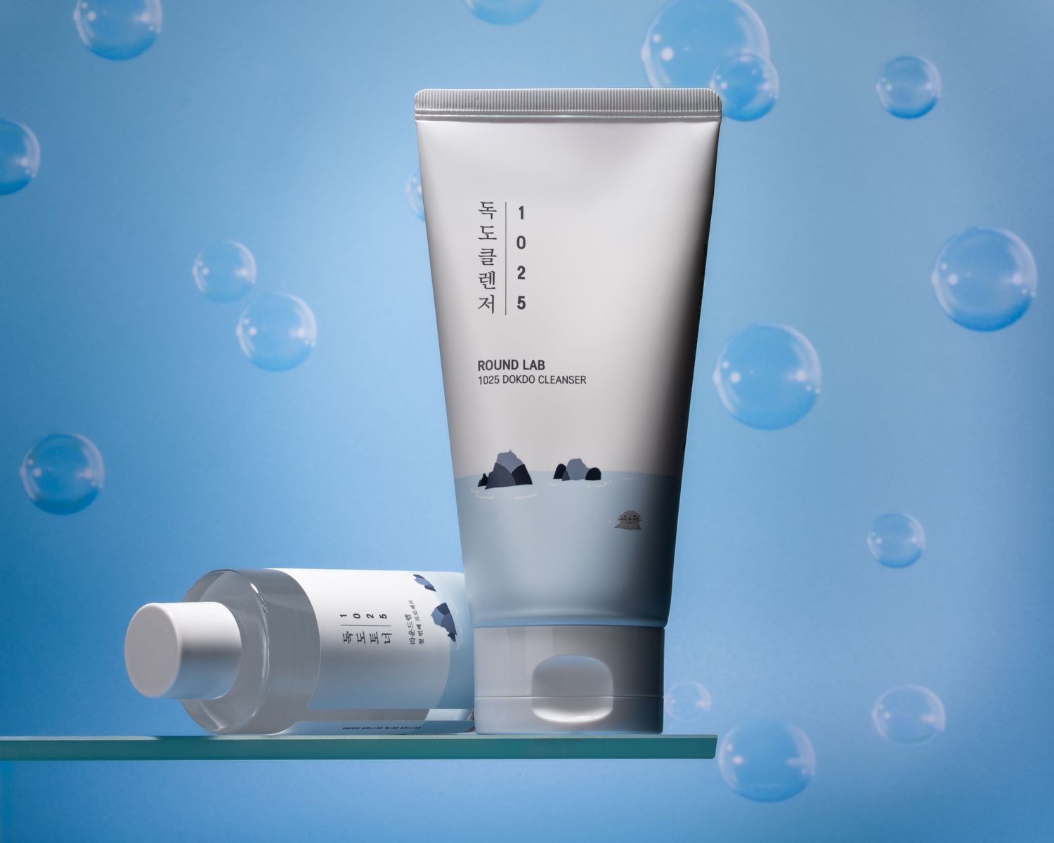 Minimalist skincare products displayed on blue backdrop with floating soap bubbles in modern cosmetic photography.