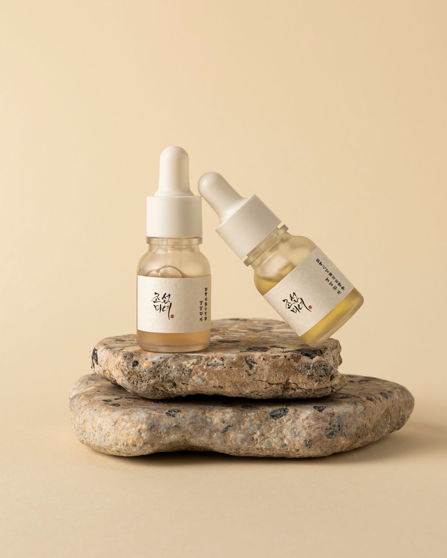 White cosmetic bottles arranged on natural stone slabs against a beige background create a minimalist beauty product display.
