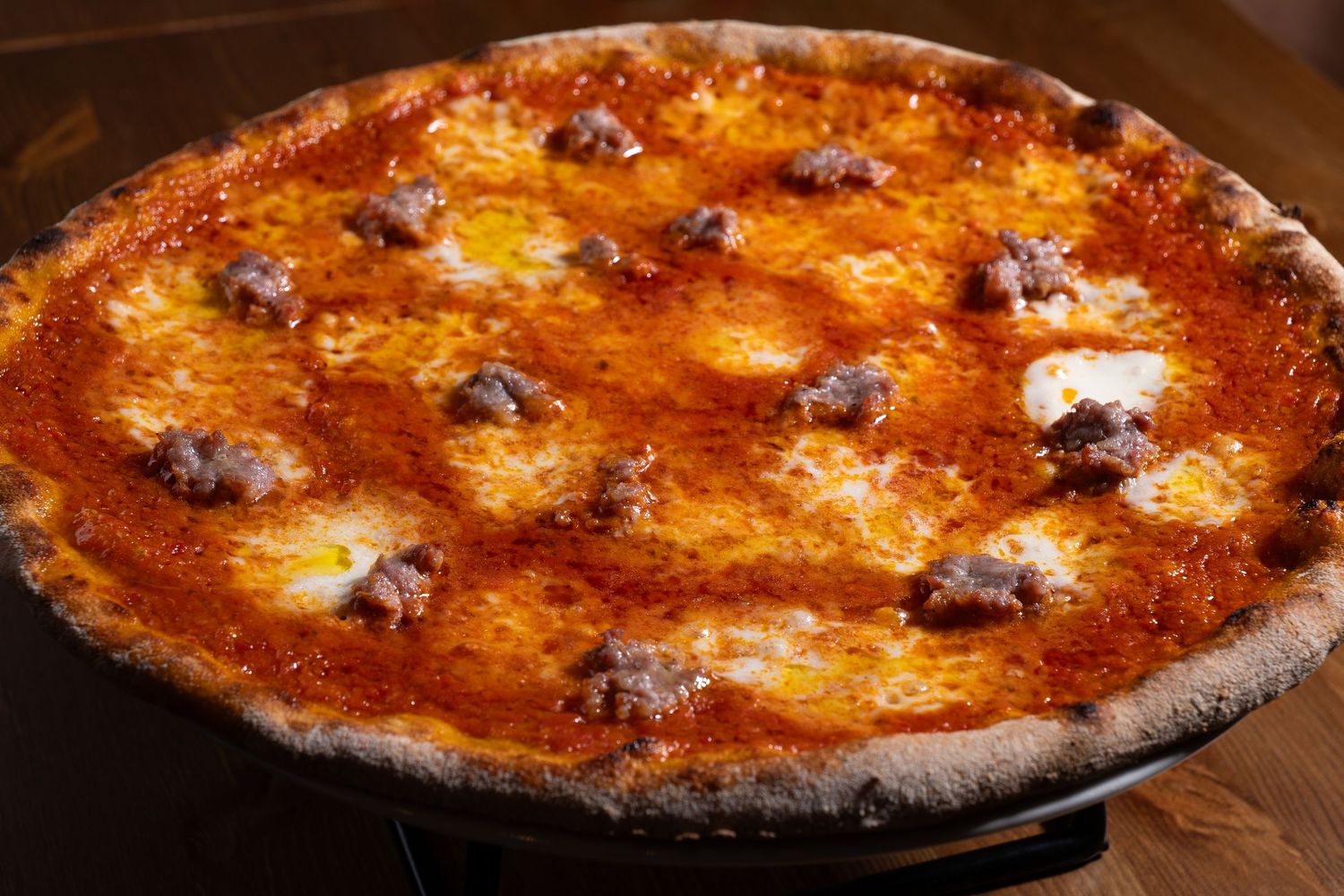 A golden-brown pizza with melted cheese and pepperoni spots on a dark charred crust, photographed from above.