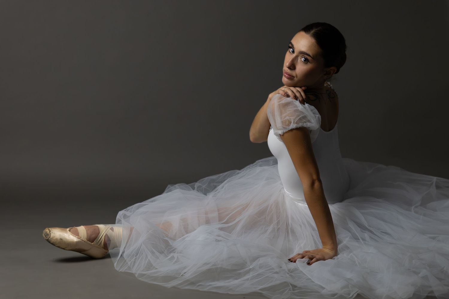 Graceful ballet dancer in white tulle dress poses on floor.