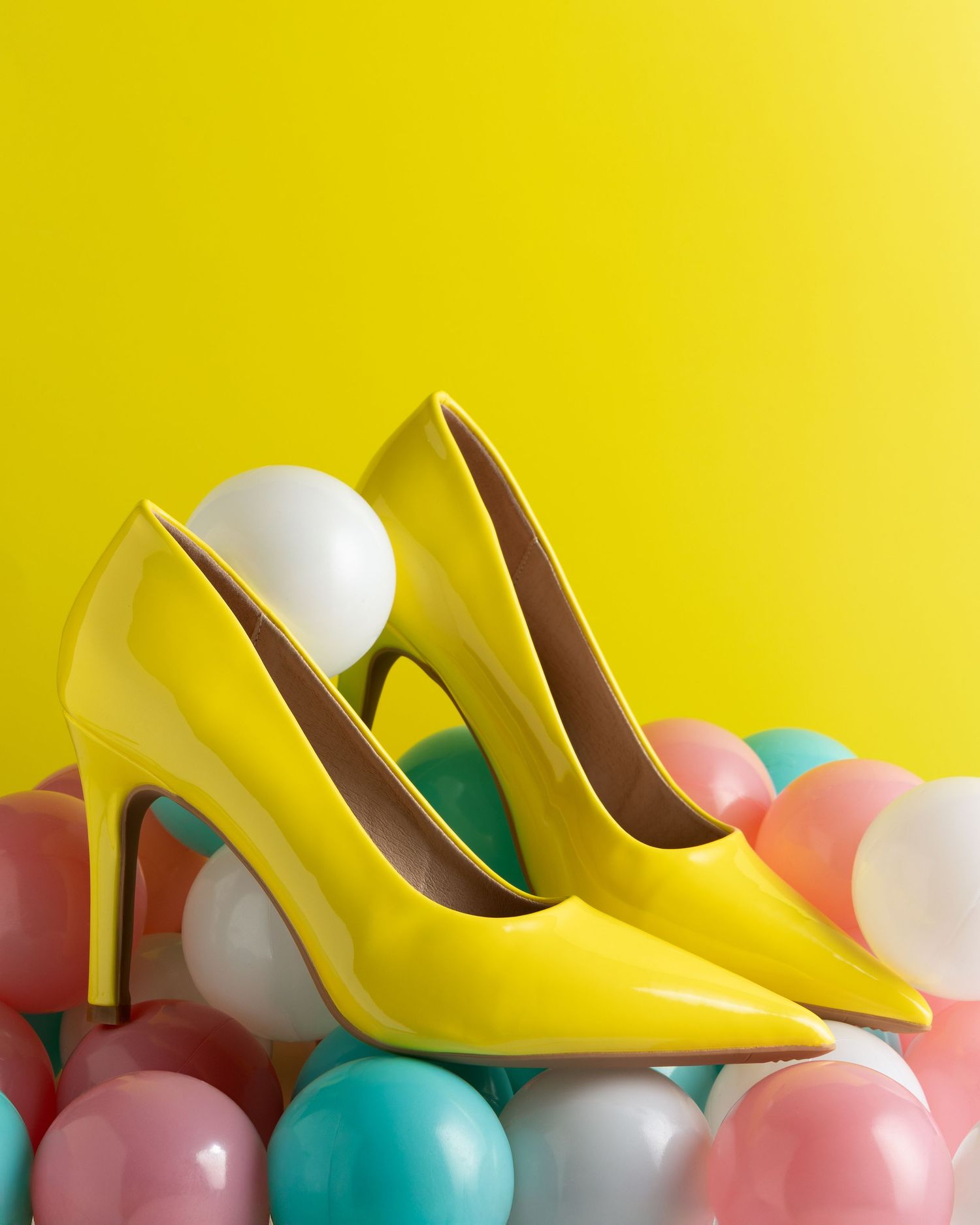 Yellow high heel shoes lined up against pastel balloons creating a festive display on yellow background.