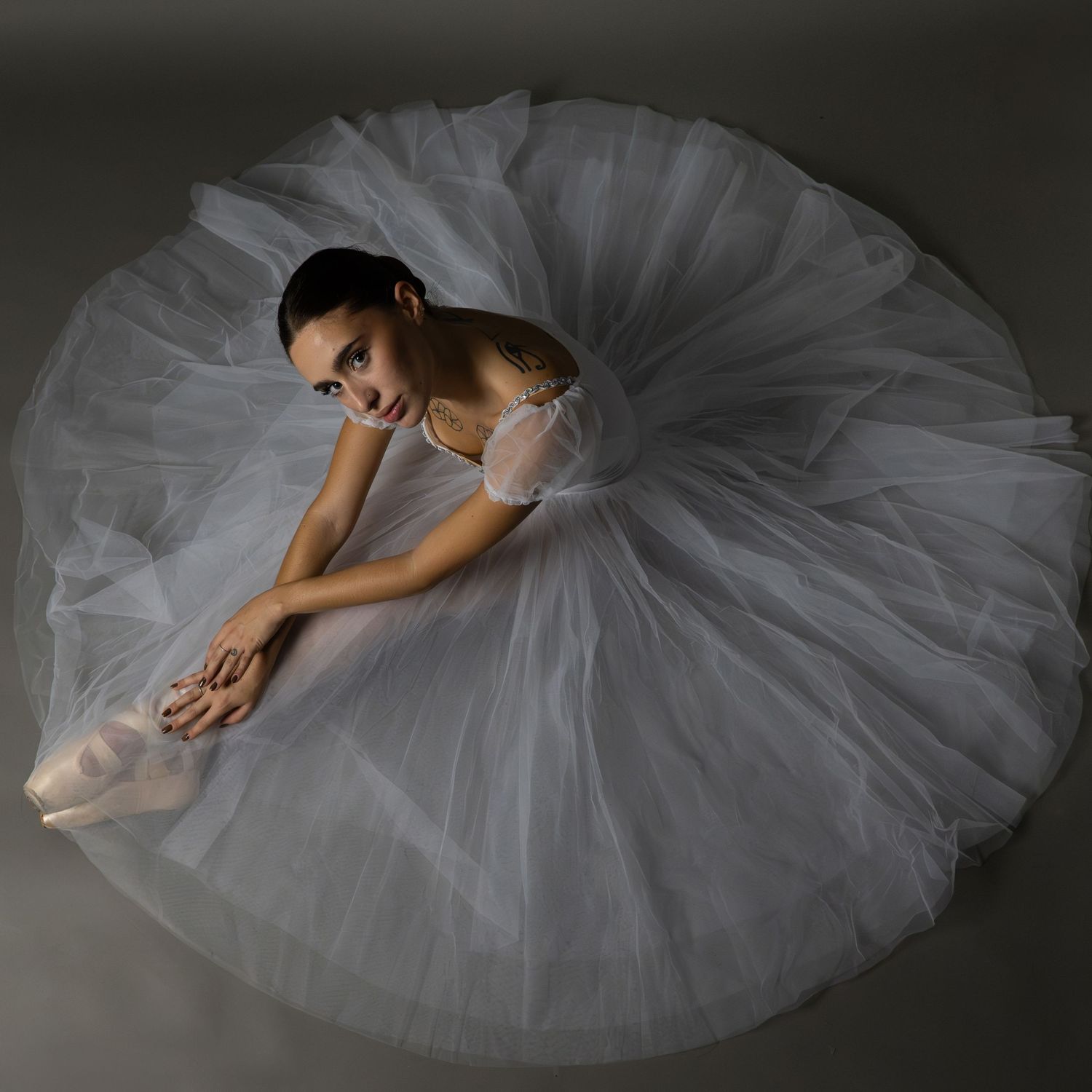 Overhead view of classical ballet dancer in white tutu on dark floor.