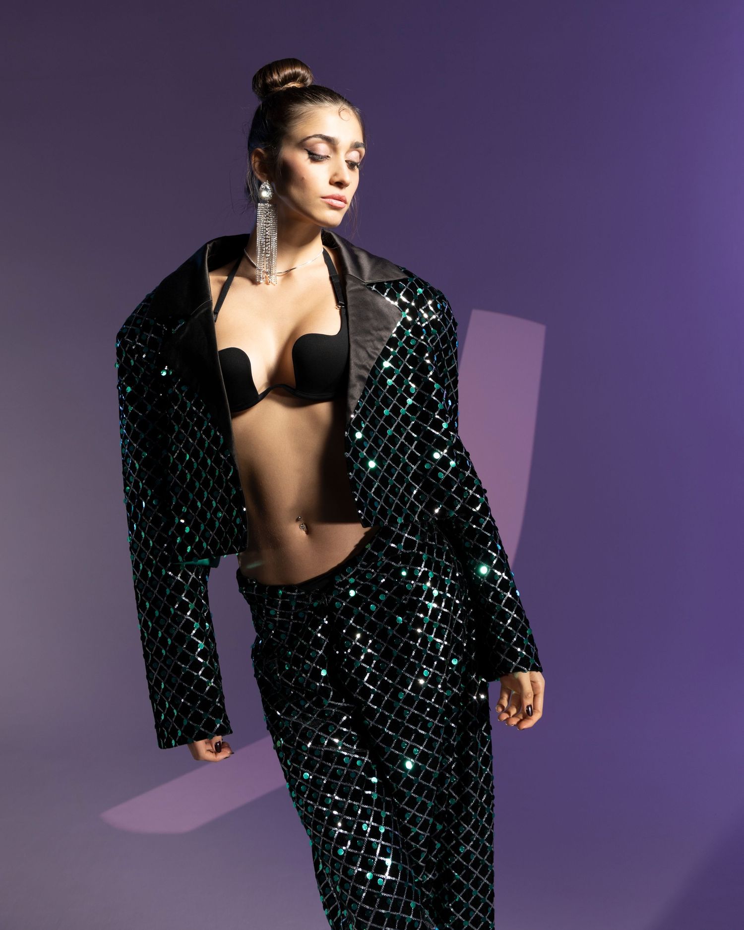 Fashion model poses in a sparkly black sequined blazer dress against a purple studio backdrop.