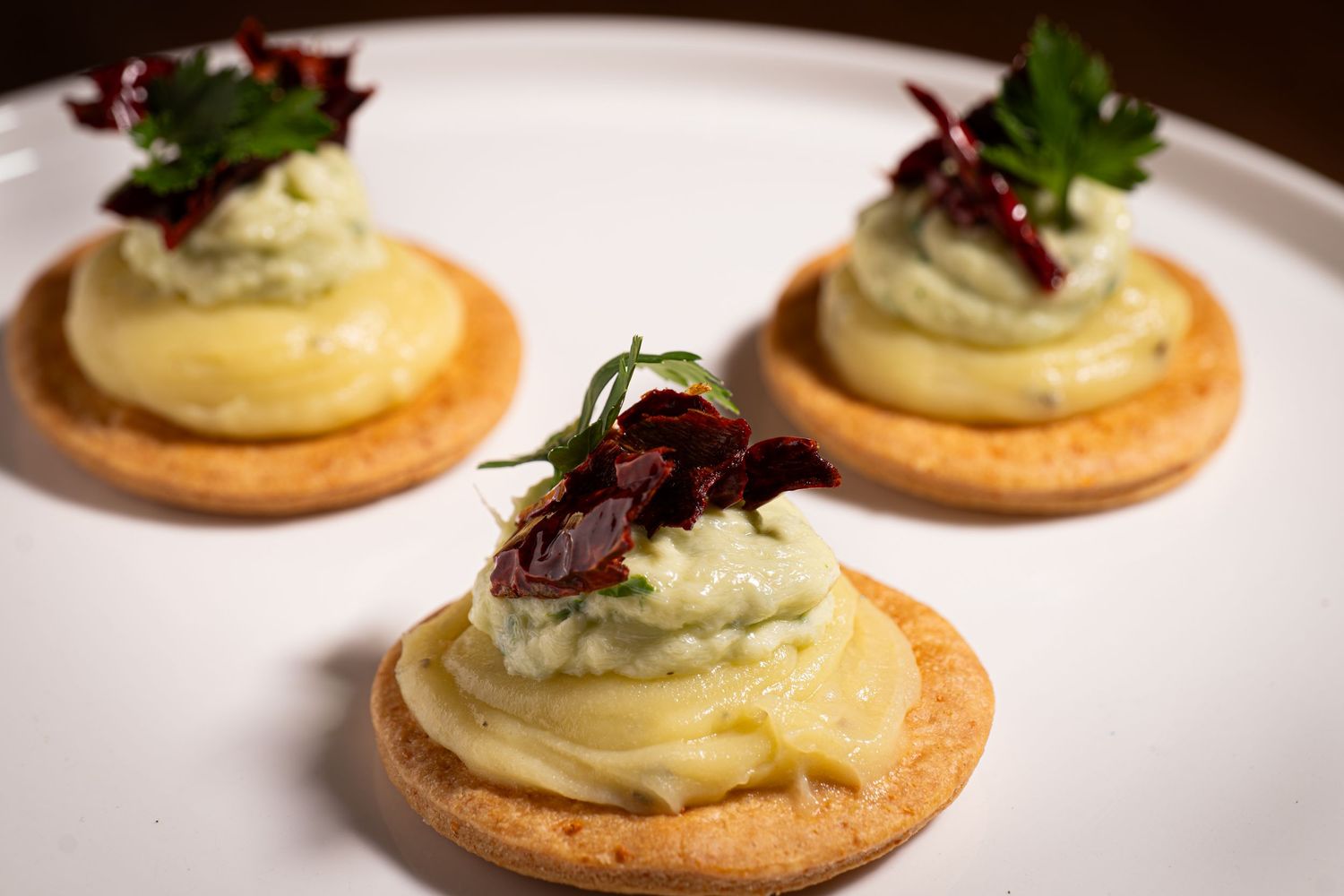 Elegant canapes with mousse and microgreens served on crispy butter crackers on a white plate.