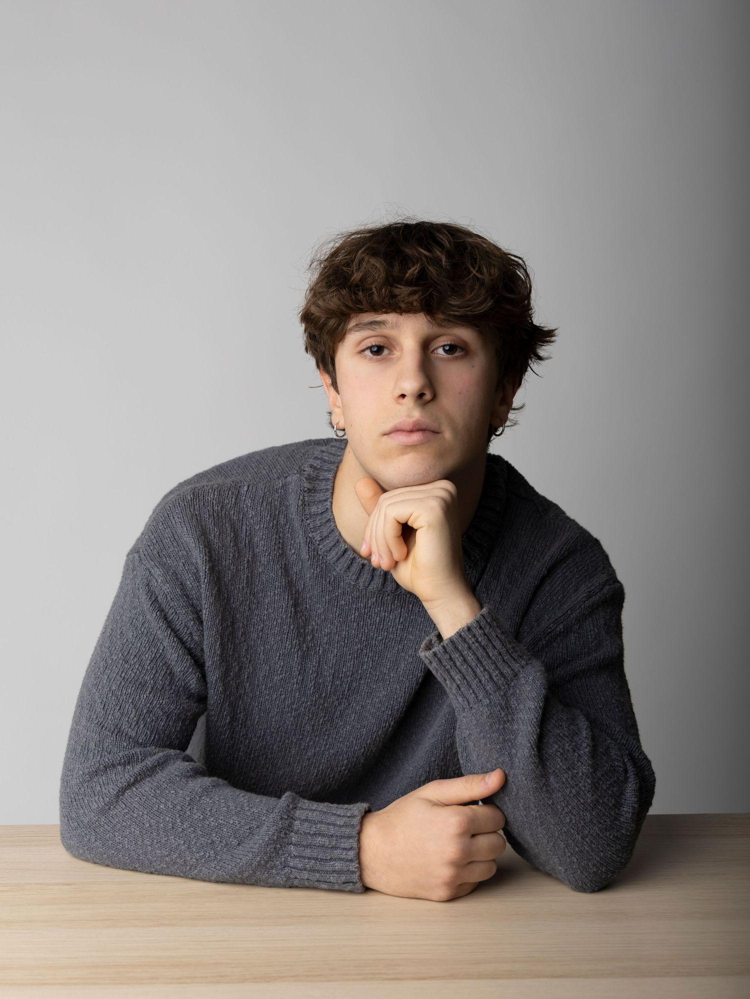 A person in a gray sweater rests their chin on their hand while lying on a wooden surface in a contemplative pose.