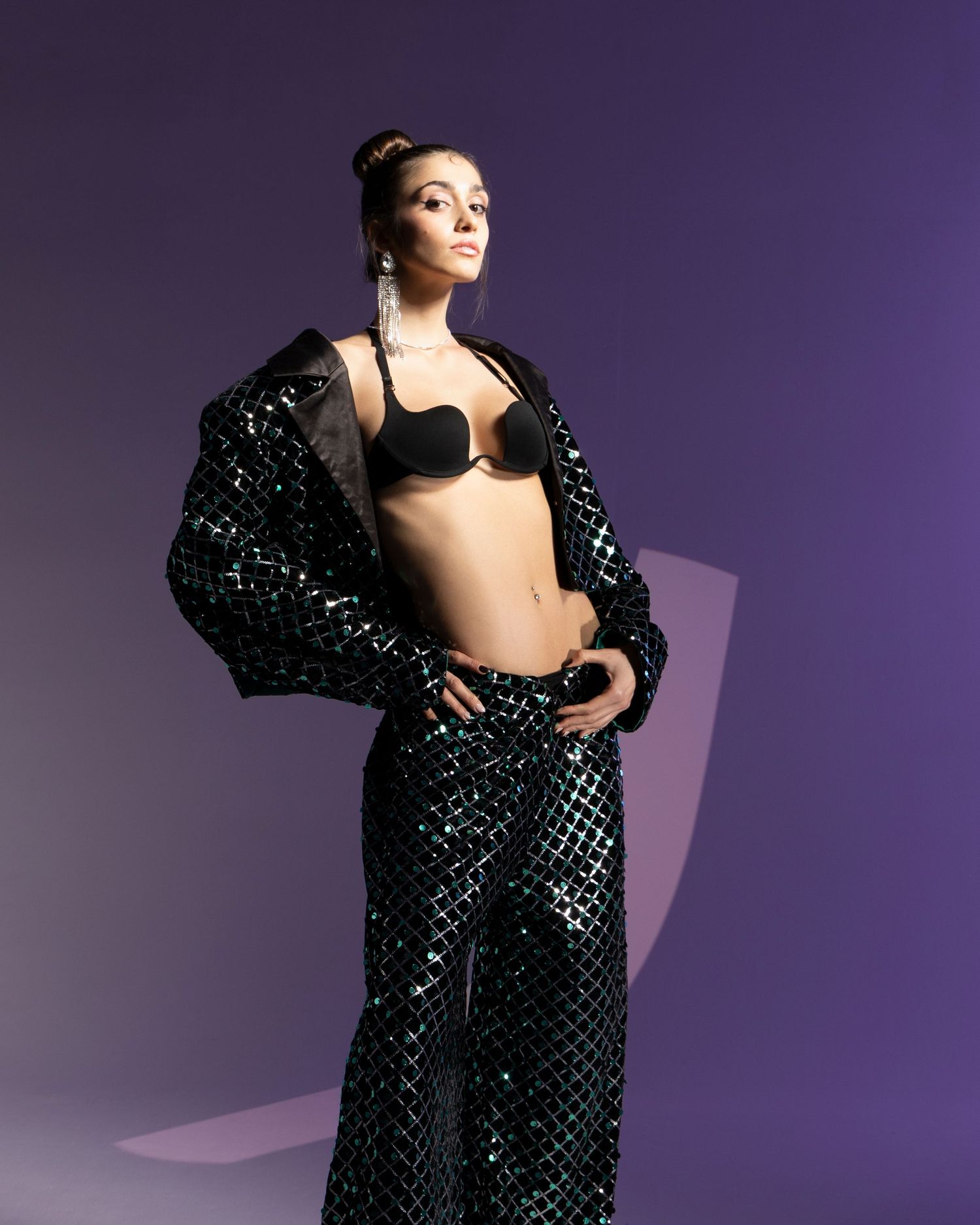 Fashion model poses in glamorous black quilted coat with dramatic puff sleeves against purple studio backdrop.