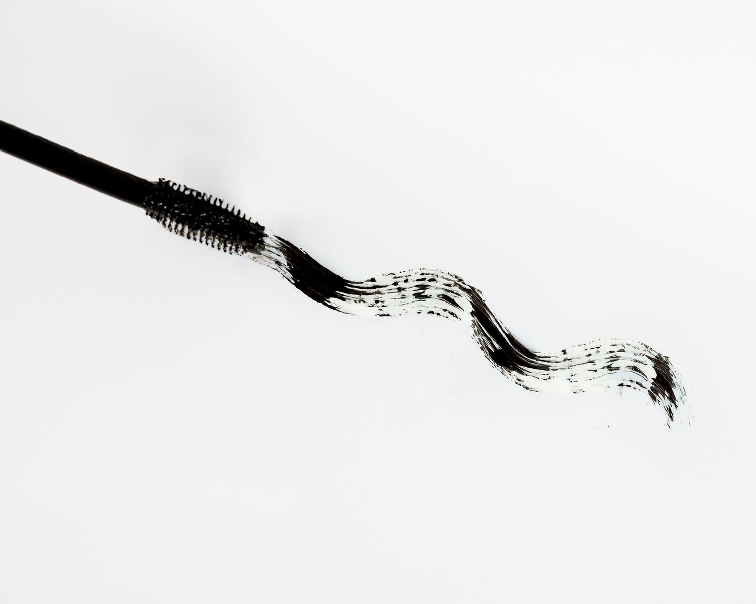 A black mascara brush with musical notes created by streaks of makeup against a white background.