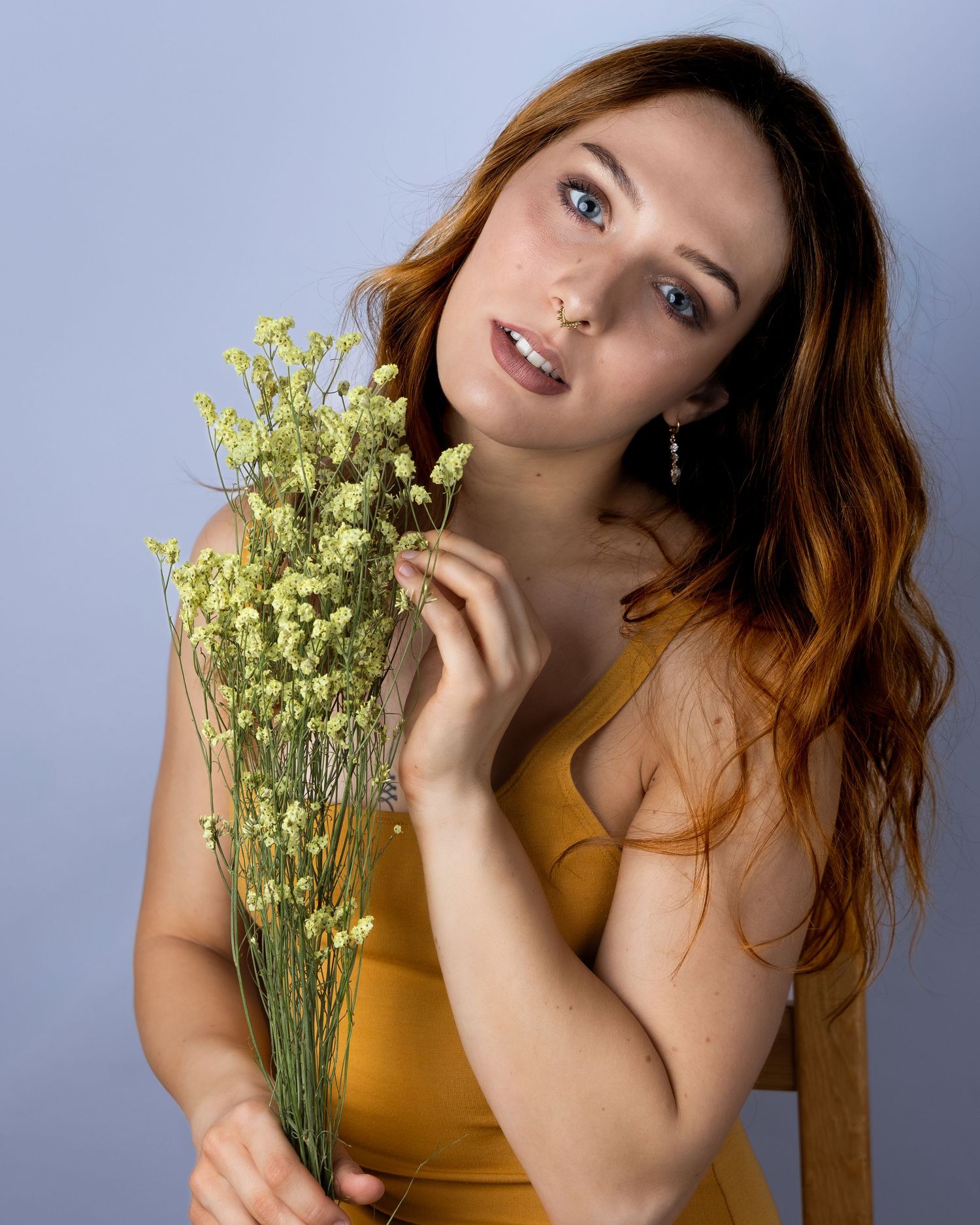 A person in a yellow tank top poses with delicate white baby's breath flowers against a gray studio backdrop.