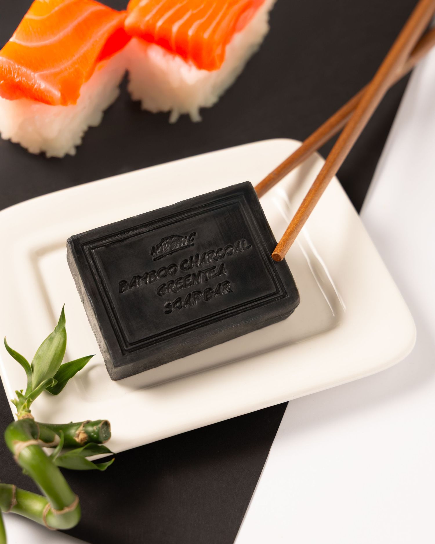 Black soap dish on white plate with chopsticks and orange salmon nigiri sushi pieces in background.