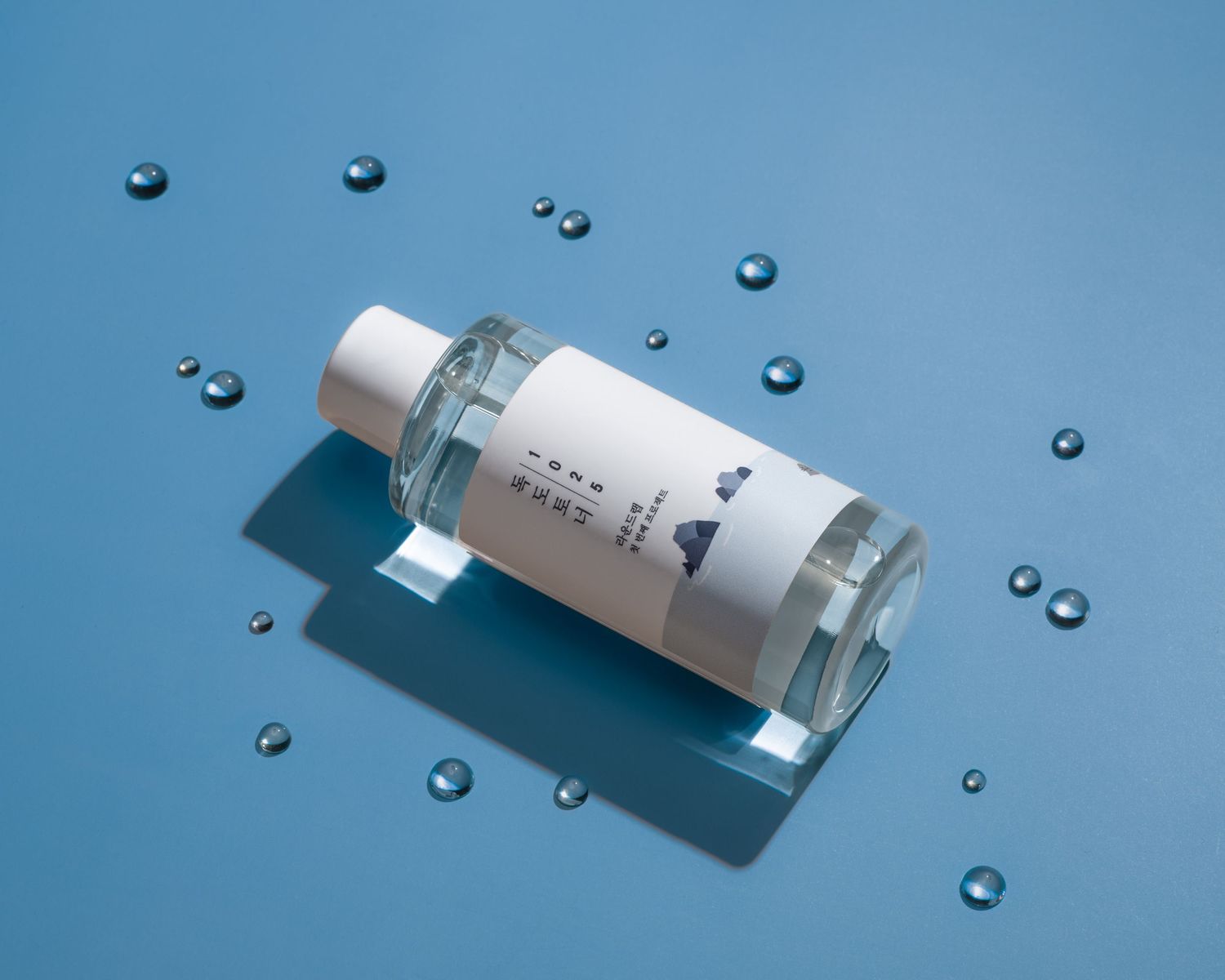 White cosmetic bottle with water droplets on blue background in minimalist product photography setup.