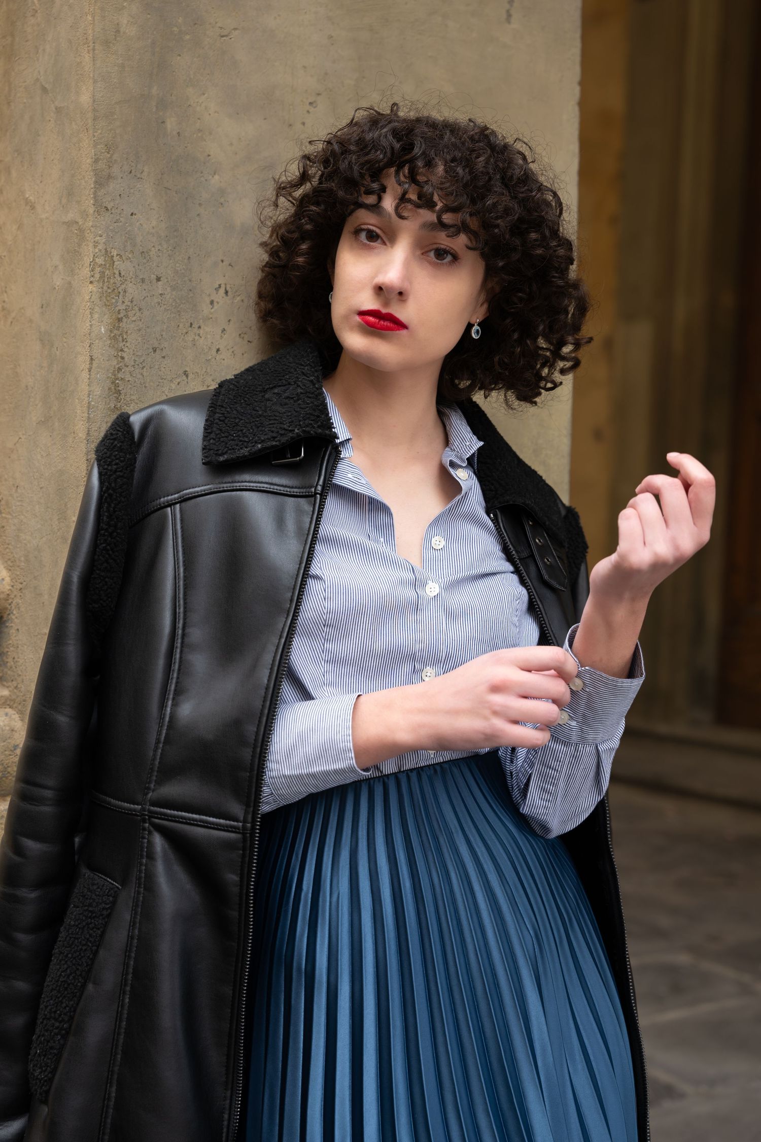 Fashion photo featuring leather jacket and pleated skirt in urban setting.
