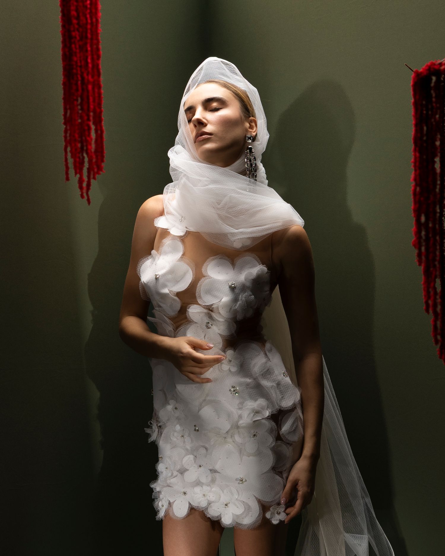 Artistic fashion photograph showing a white tulle dress with cloud-like ruffles against a dark green background.