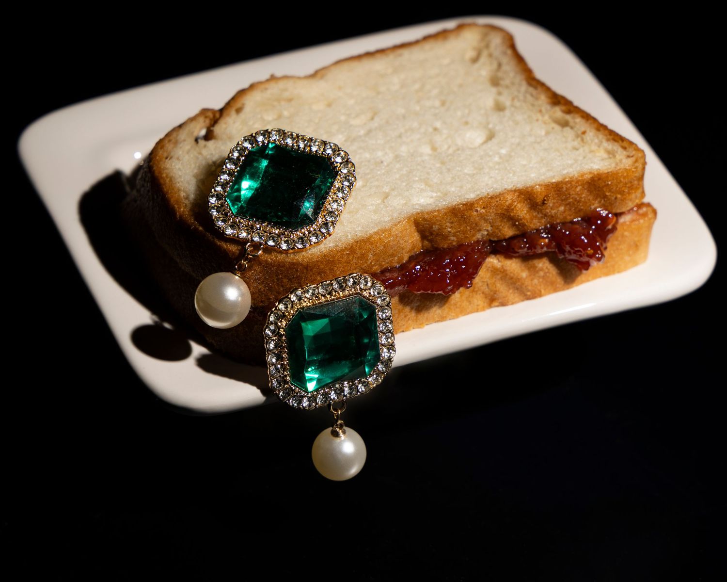 A vintage emerald and pearl brooch photographed in sequence being placed on slices of white bread against black background.