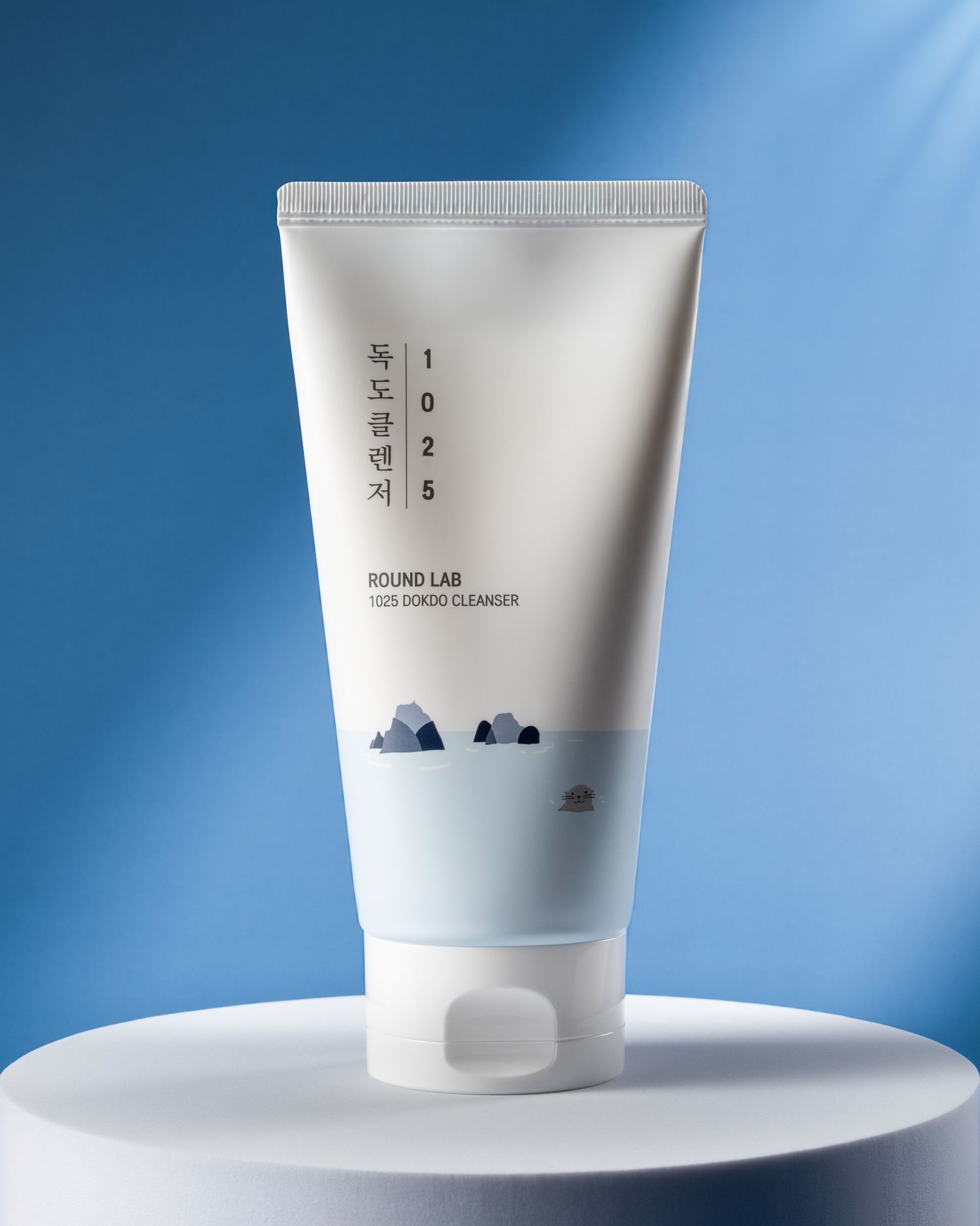 A white skincare cleanser tube with minimal Asian text design and mountain illustrations on a blue background.
