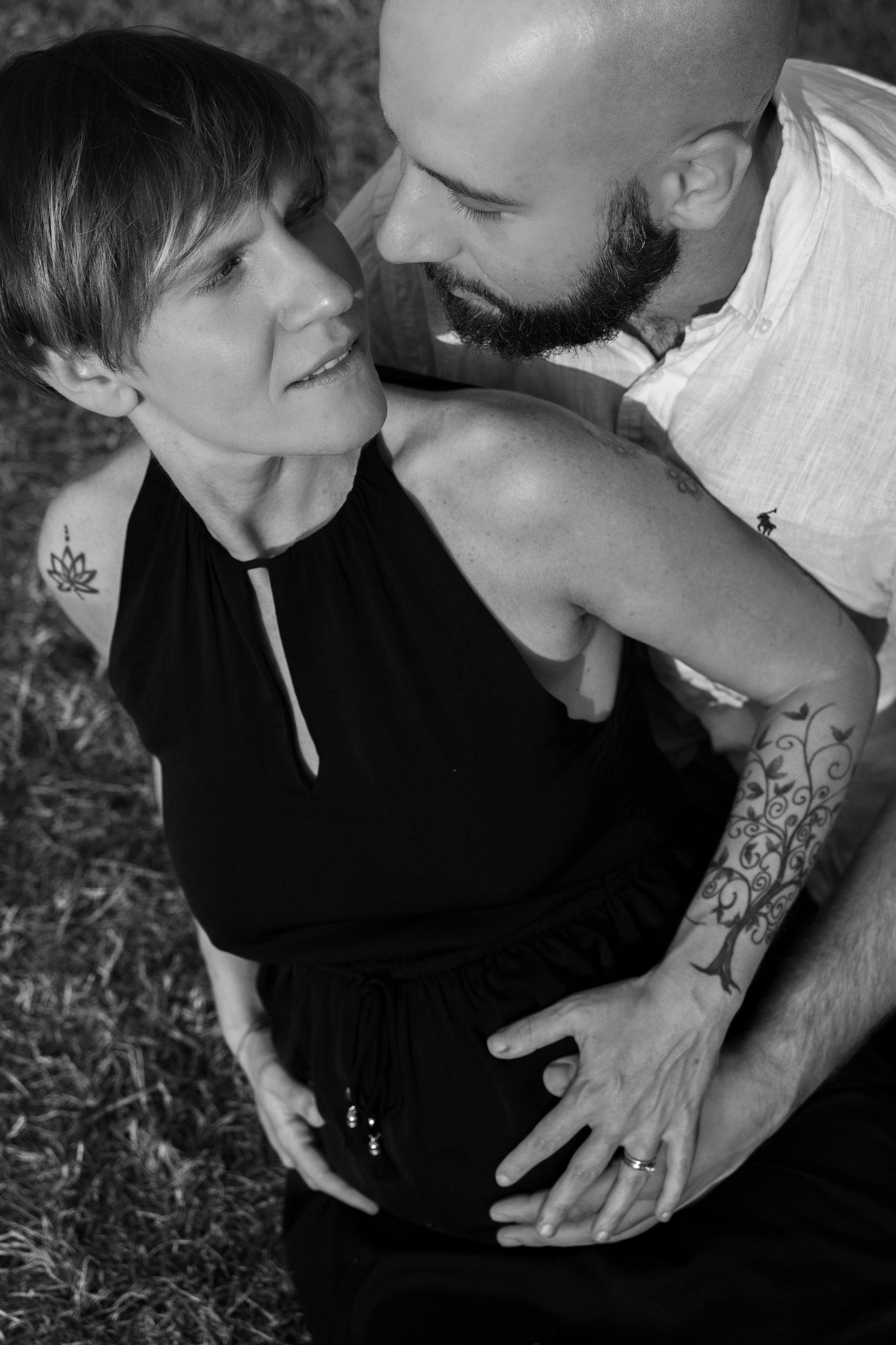 Black and white intimate portrait of a couple in loving embrace outdoors, showing tattoos and tender connection.