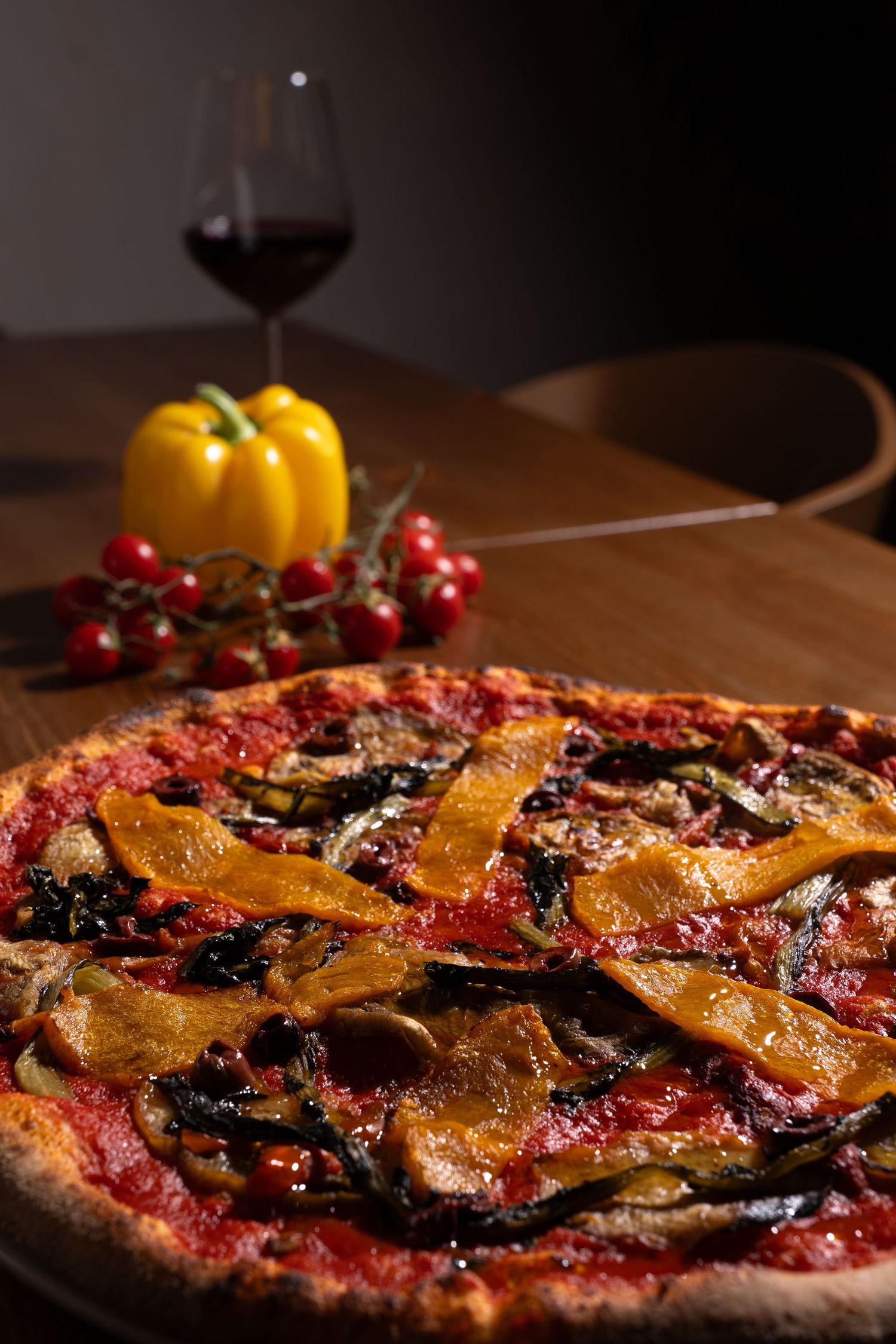 A rustic homemade pizza with roasted bell peppers, eggplant slices and tomato sauce on a wooden surface.