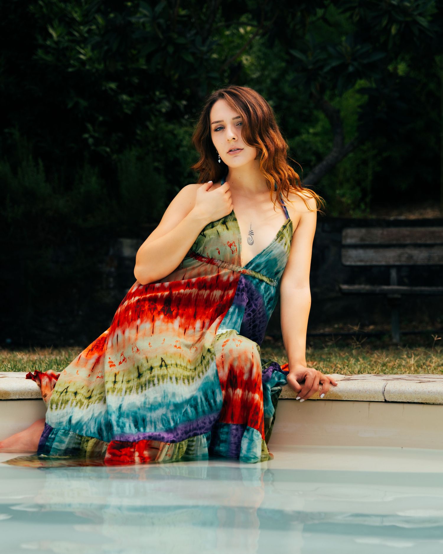 Woman in tie-dye dress lounging gracefully along the edge of a swimming pool on a summer day.