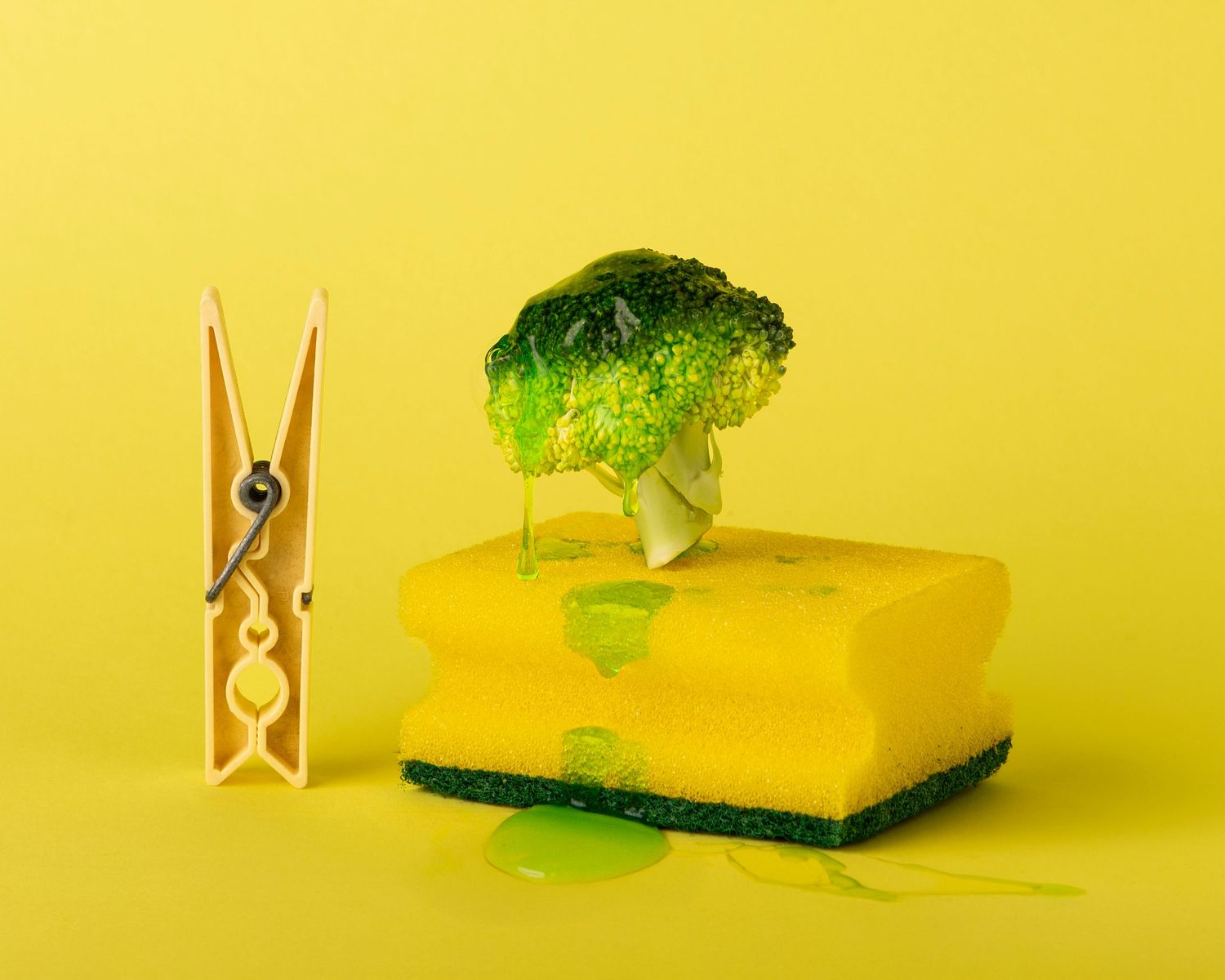 Wooden clothespin and green broccoli floret casting shadows on bright yellow background in minimalist composition.