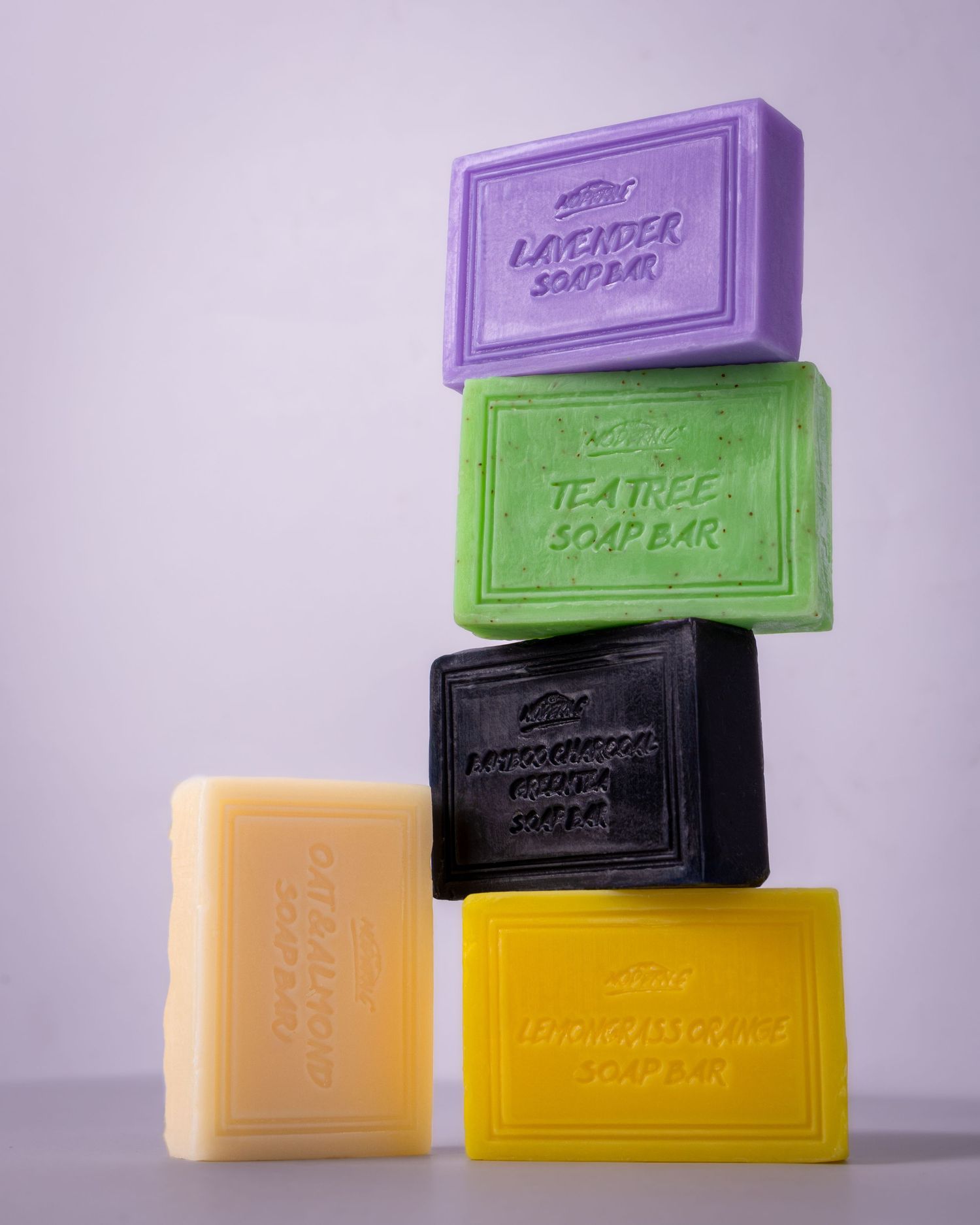 A stack of colorful artisanal soap bars in purple, green, black, orange and yellow arranged in a minimalist composition.