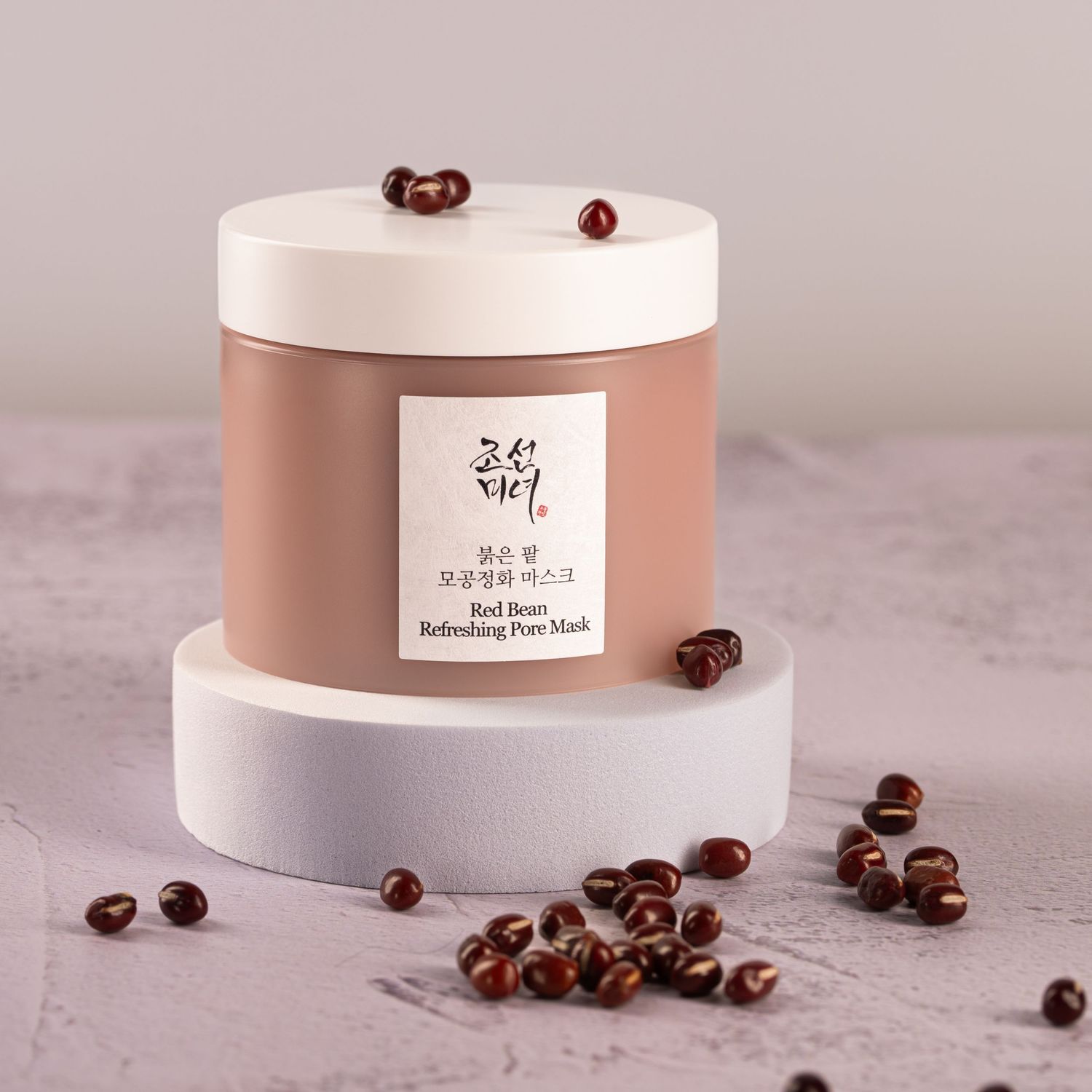 Korean beauty product jar in rose gold with coffee beans scattered around on gray surface.